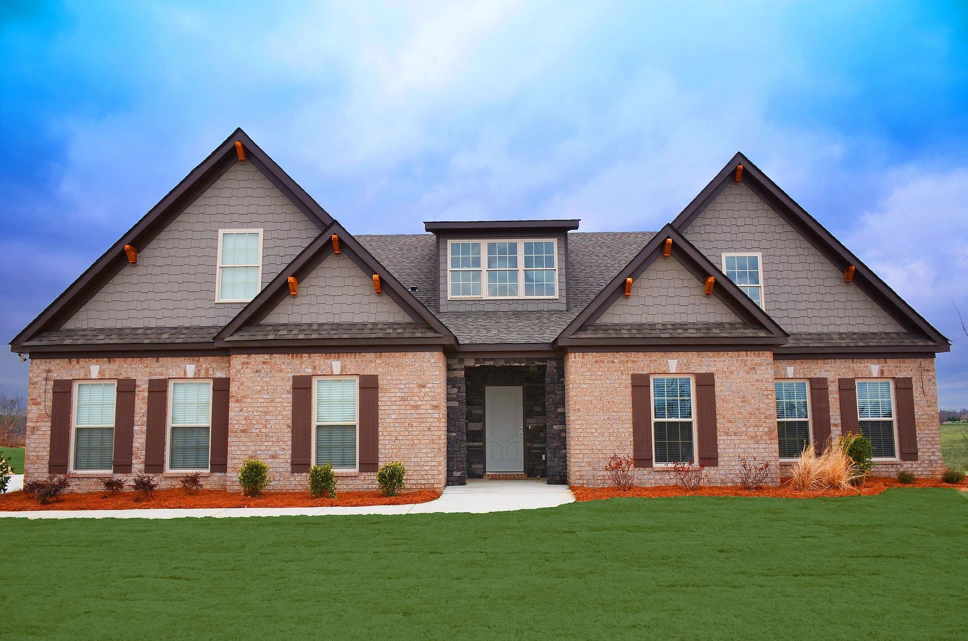 A large brick house with brown shutters and a blue sky in the background