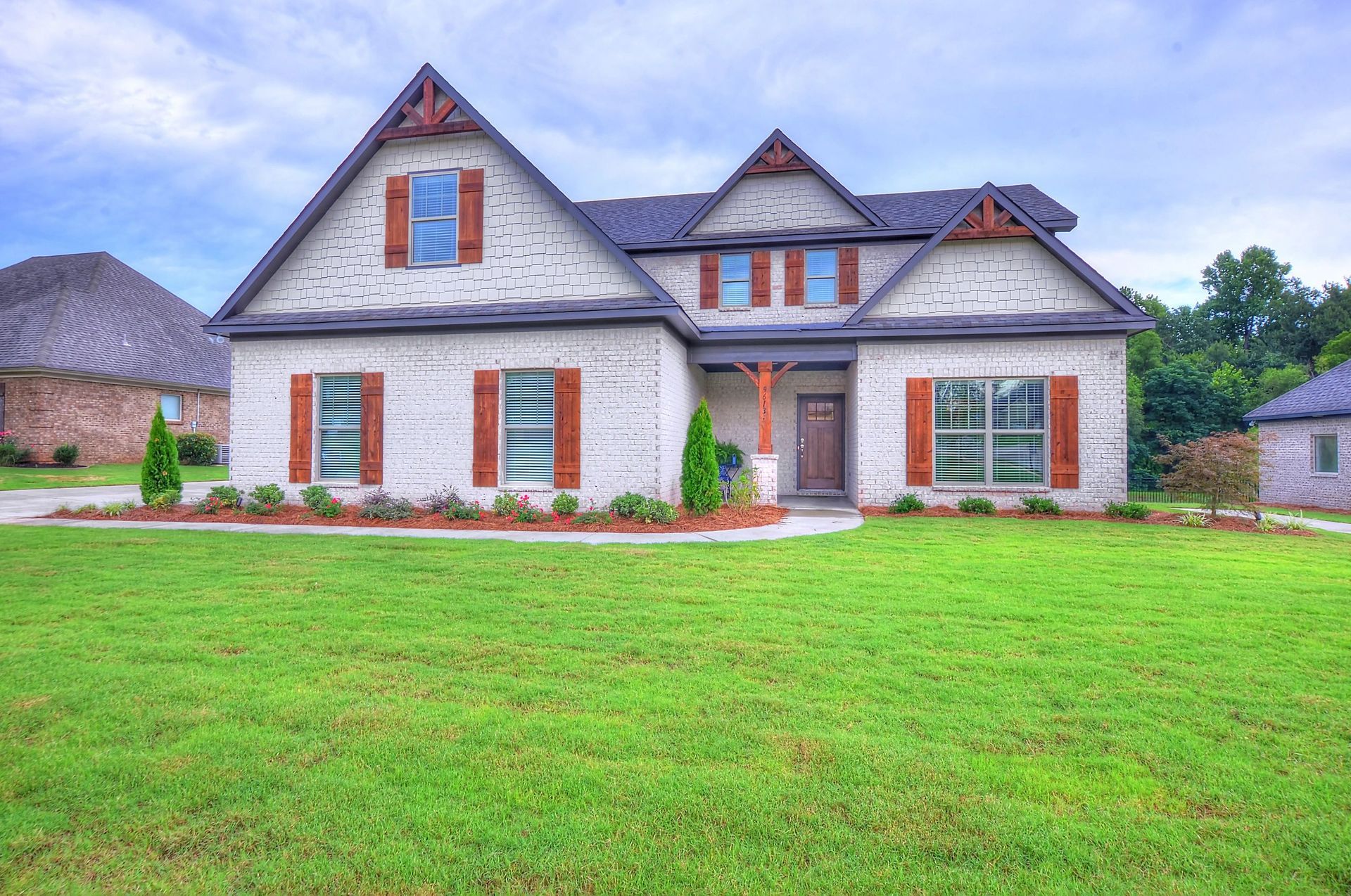 A large white brick house with a lush green lawn in front of it.