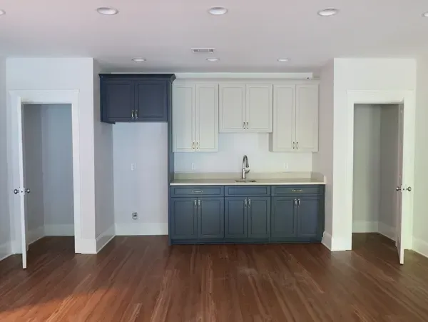 An empty kitchen with a sink , cabinets , and hardwood floors.