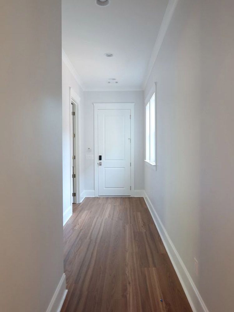 A long hallway with hardwood floors and white walls leading to a door.