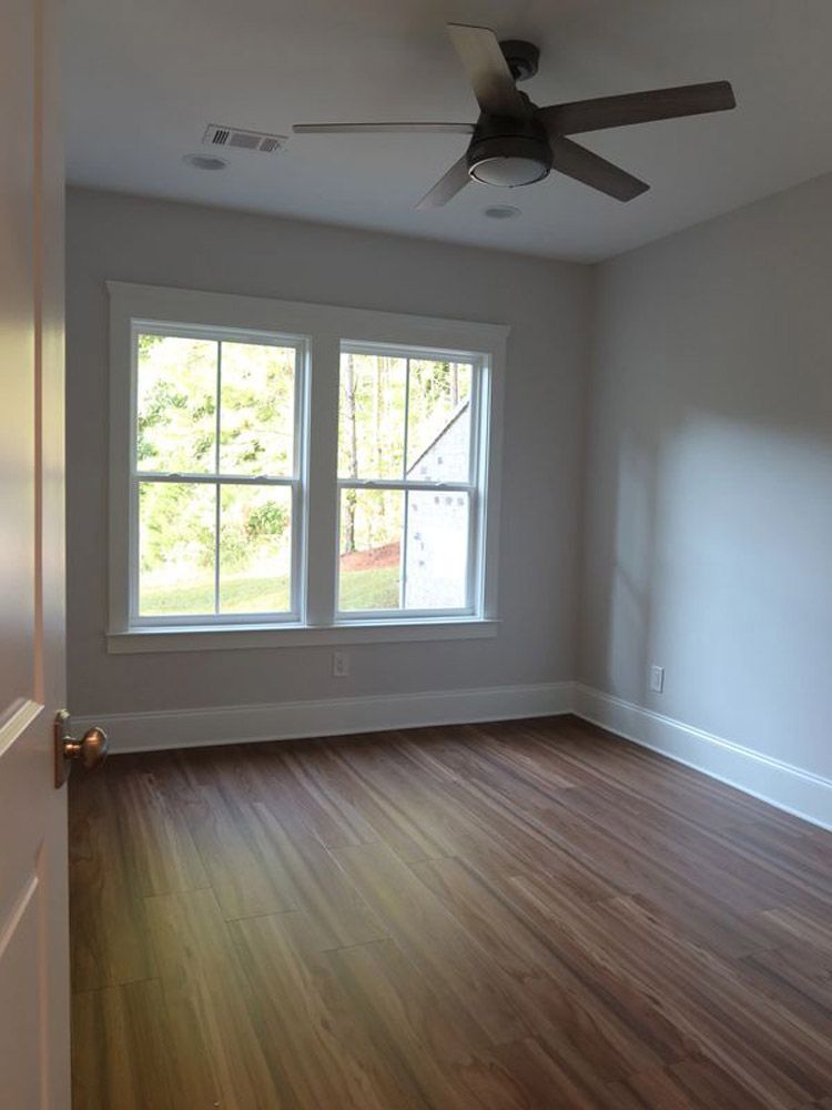 An empty room with a ceiling fan and two windows.