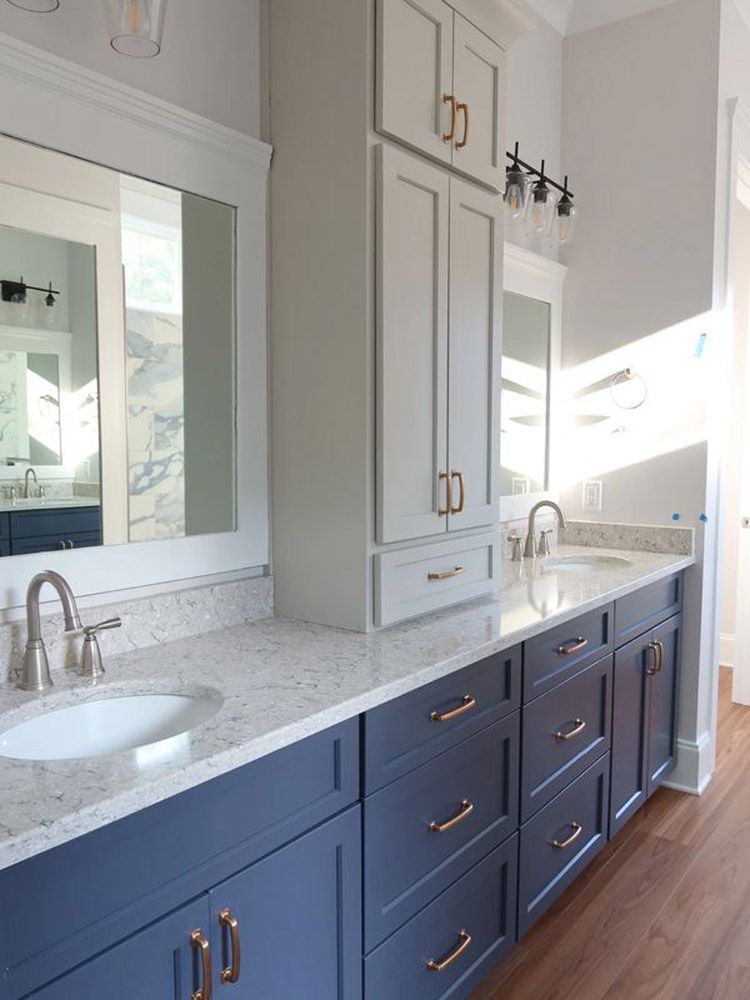A bathroom with blue cabinets , white counter tops , a sink and a mirror.