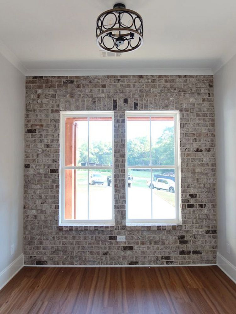 An empty room with a brick wall and two windows.