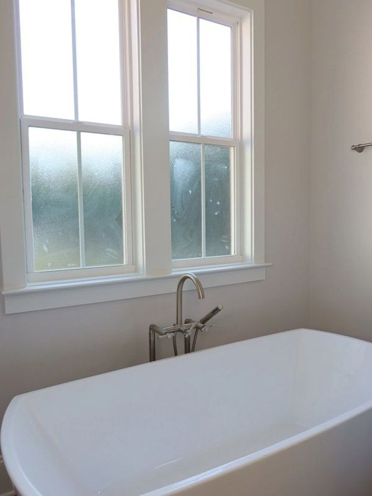 There is a bathtub in the bathroom with two windows.