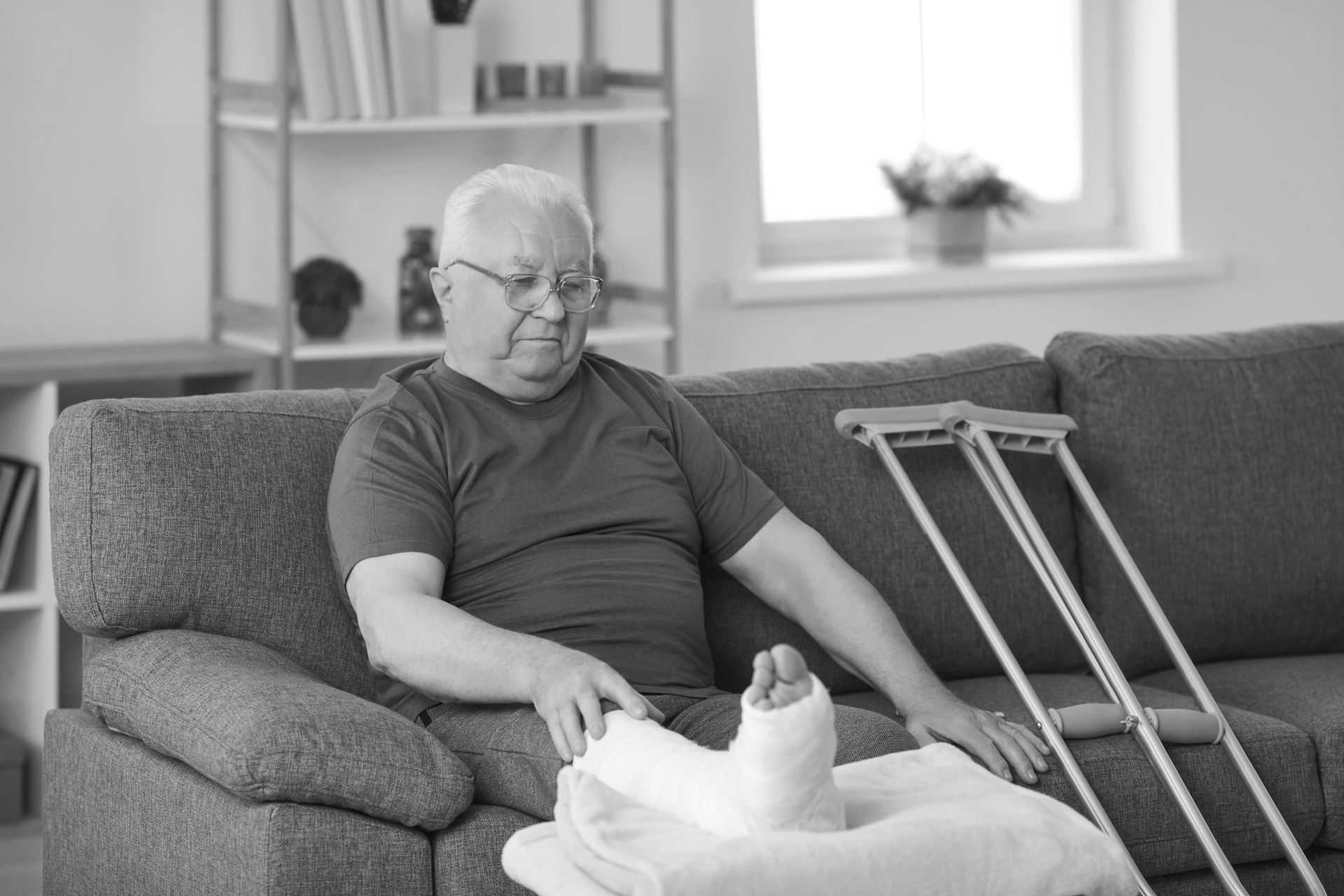 A man with a cast on his leg is sitting on a couch with crutches.
