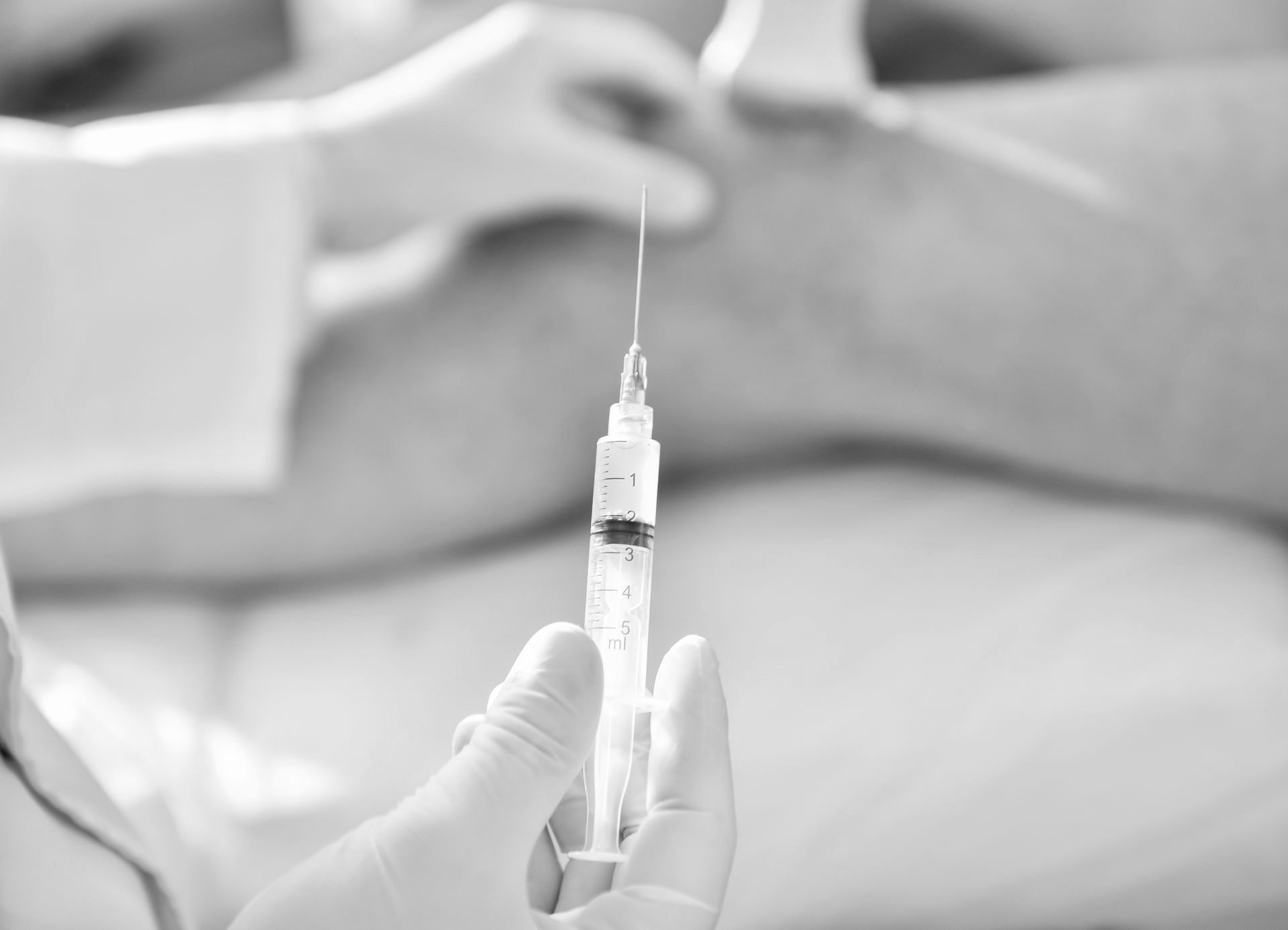 A person is holding a syringe in their hand in a black and white photo.