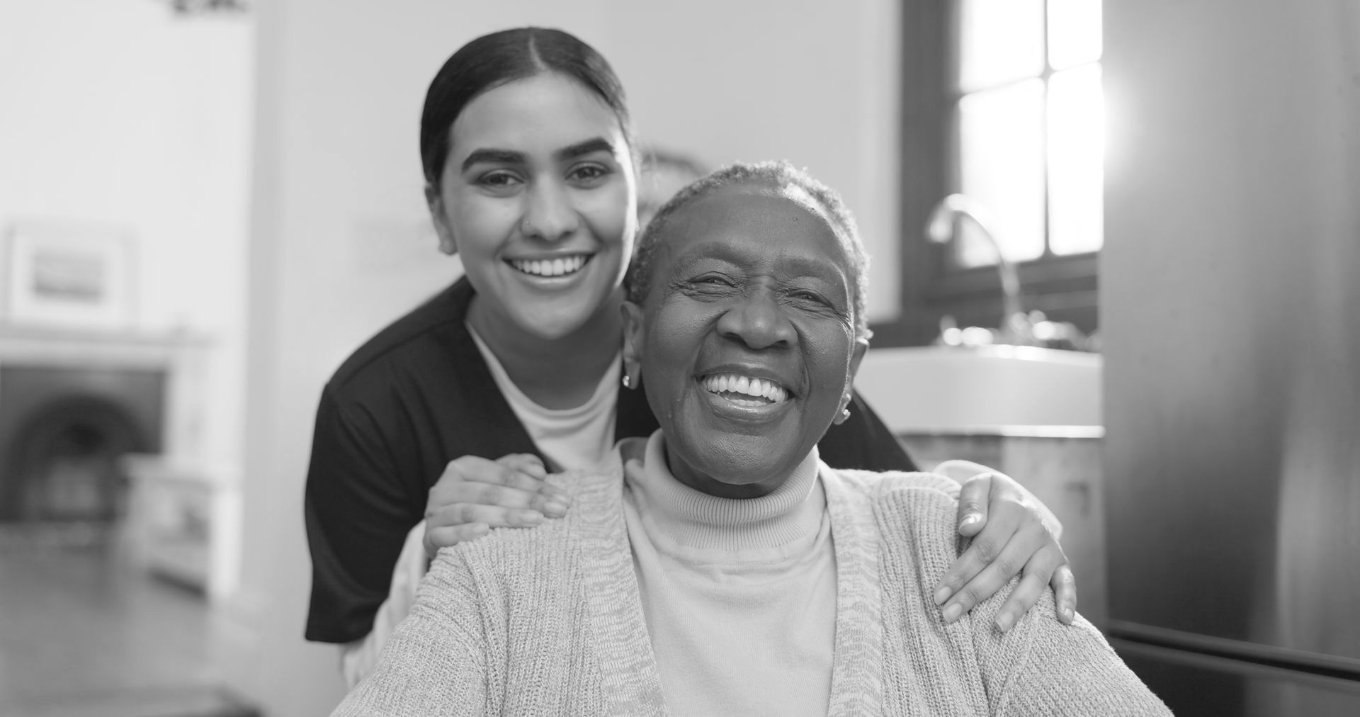 A black and white photo of an elderly woman and a young woman smiling for the camera.