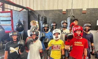 A group of young boxers wearing helmets and gloves in a gym. Some are smiling, ready to spar.
