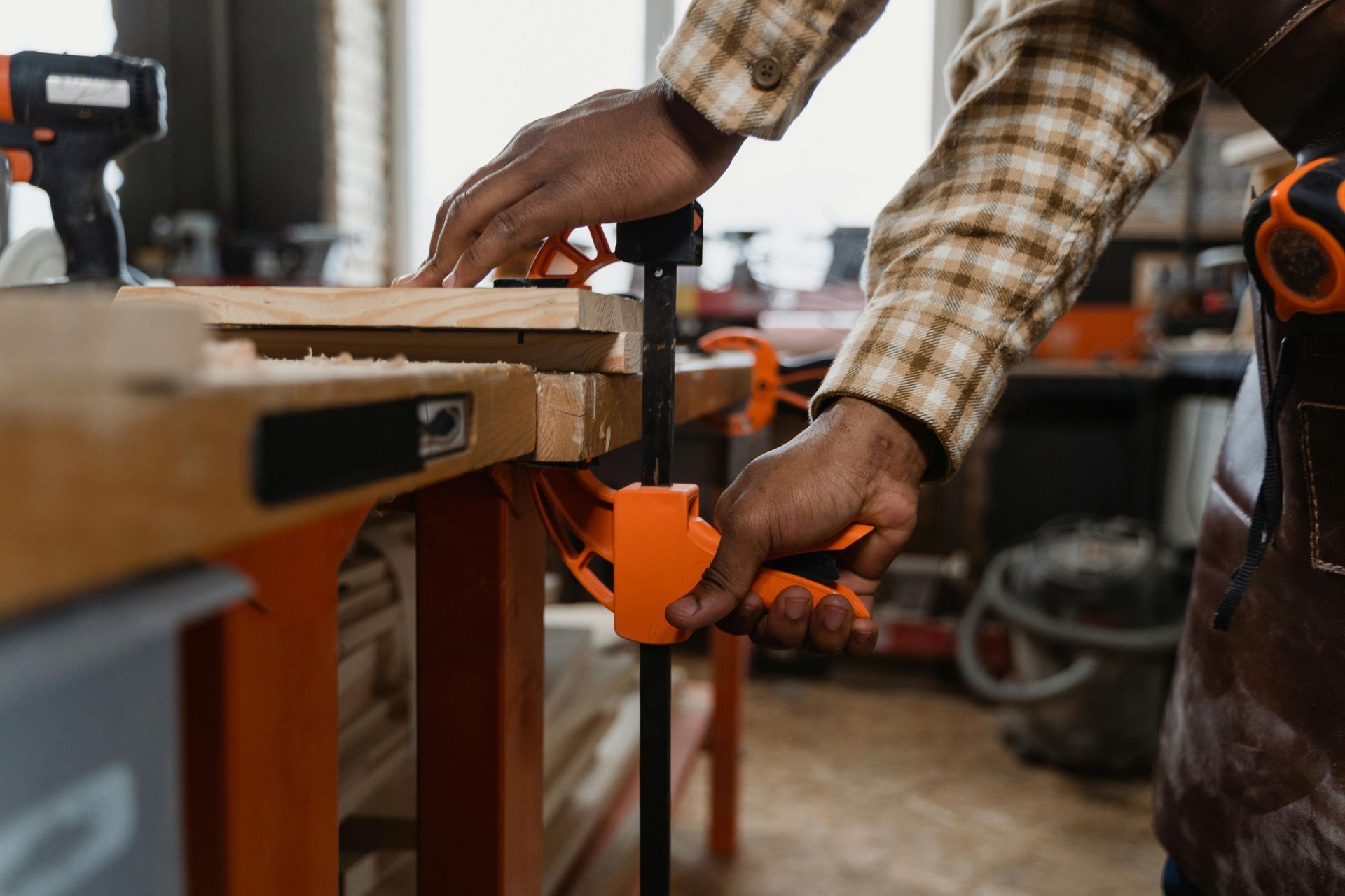Person clamps wood pieces on a workbench in a workshop. Orange clamp in use.