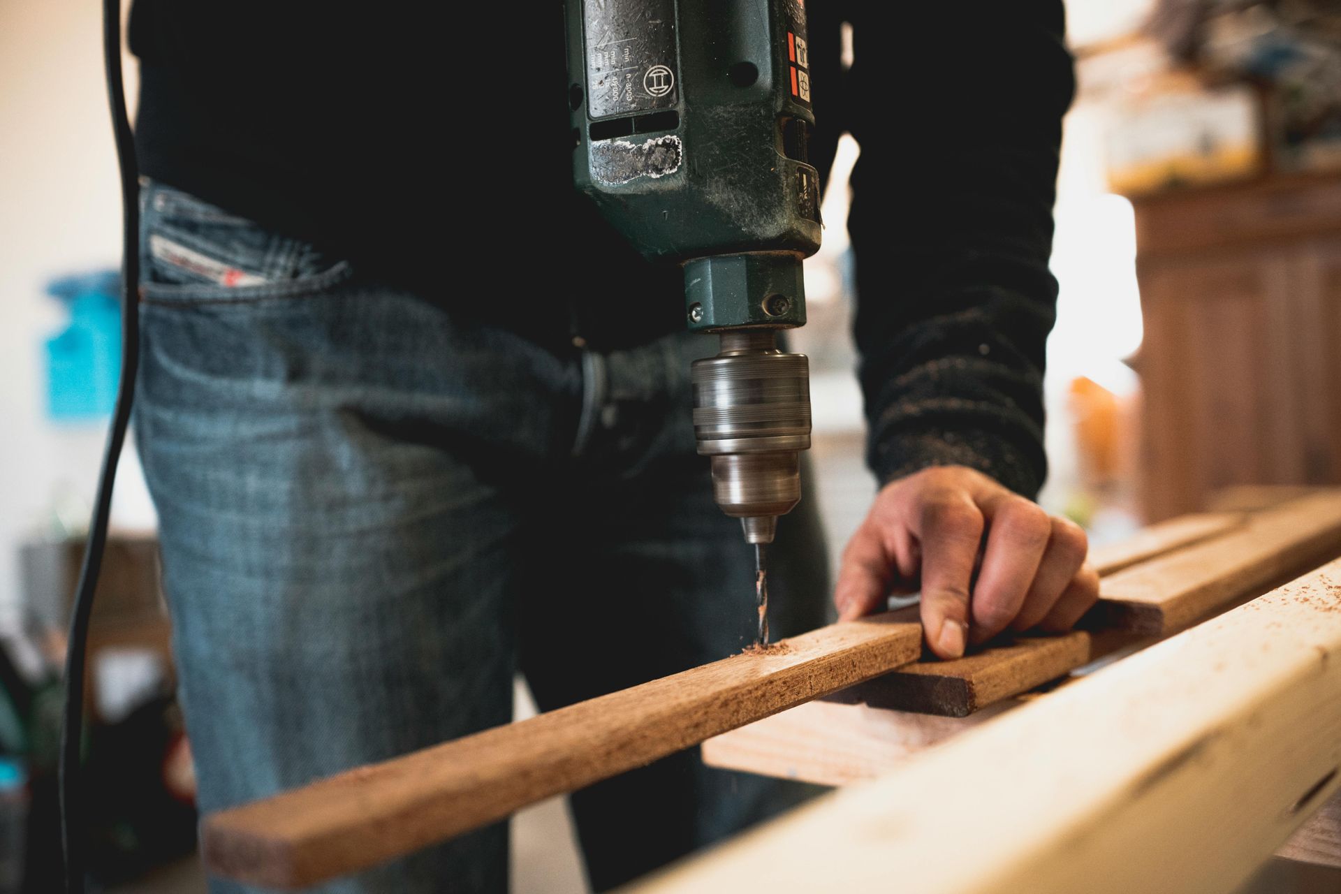 A construction worker using a drill to make a hole in a piece of wood on a workbench.