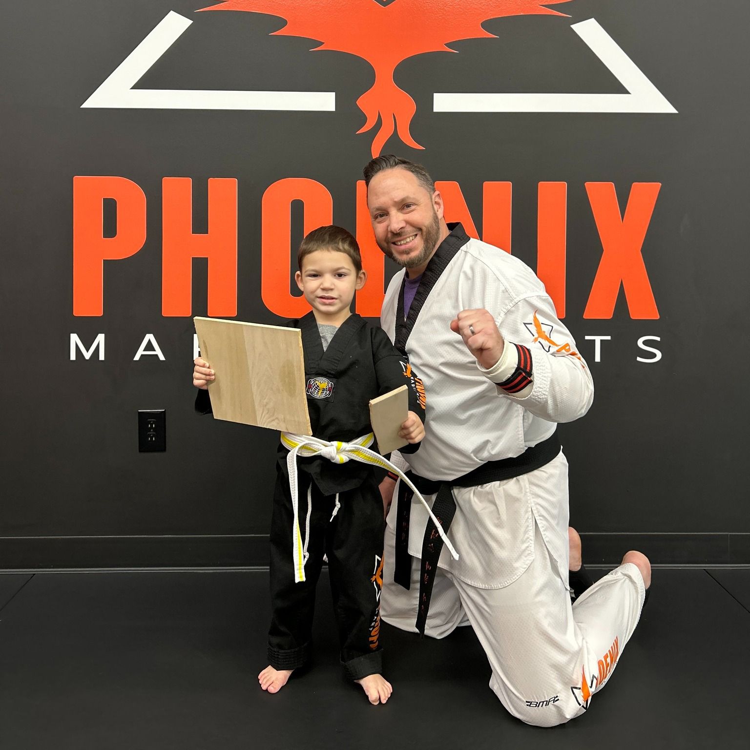 A man and a boy are posing for a picture in front of a sign that says phoenix martial arts.
