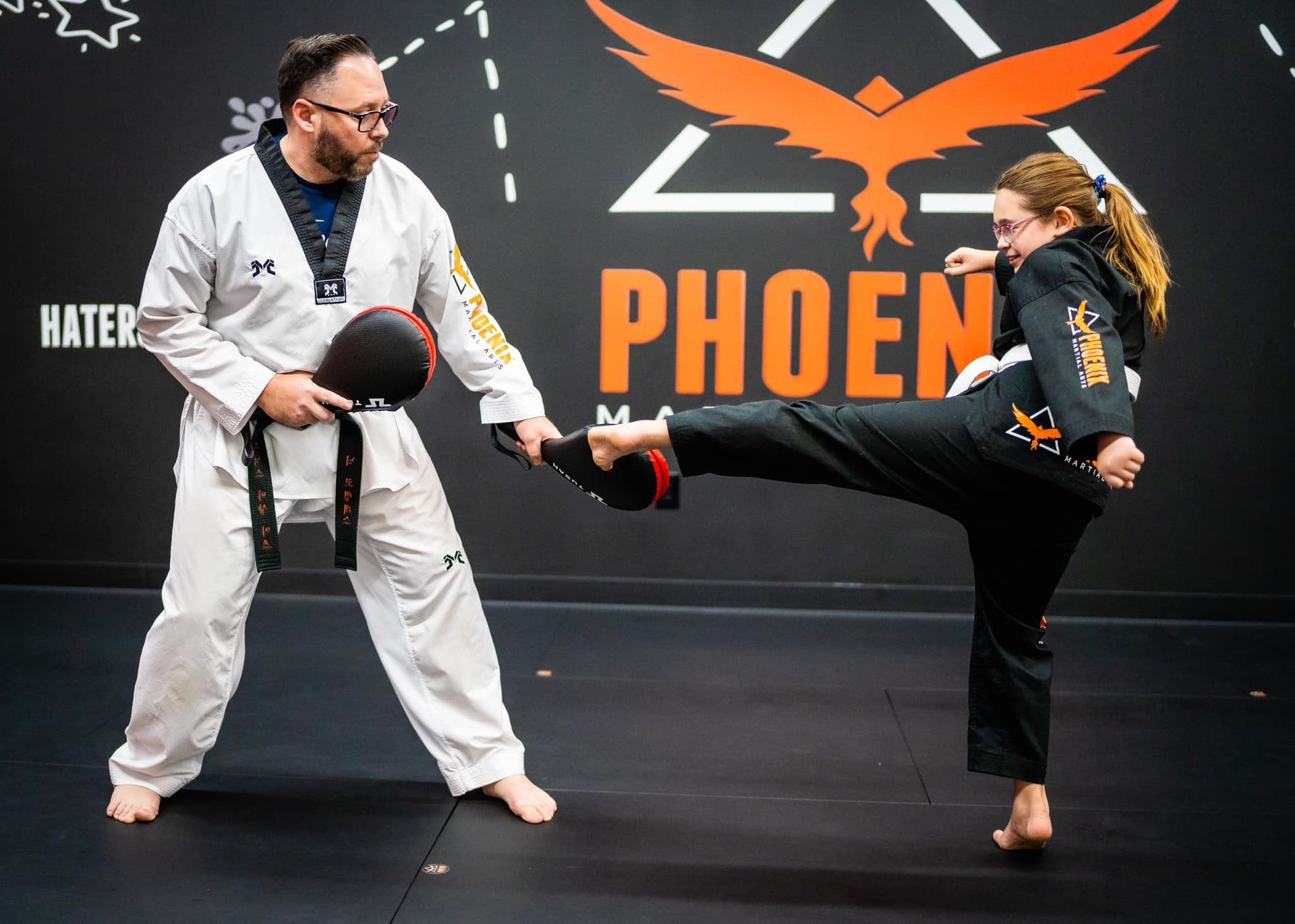 A man and a girl are practicing martial arts in front of a sign that says phoen.