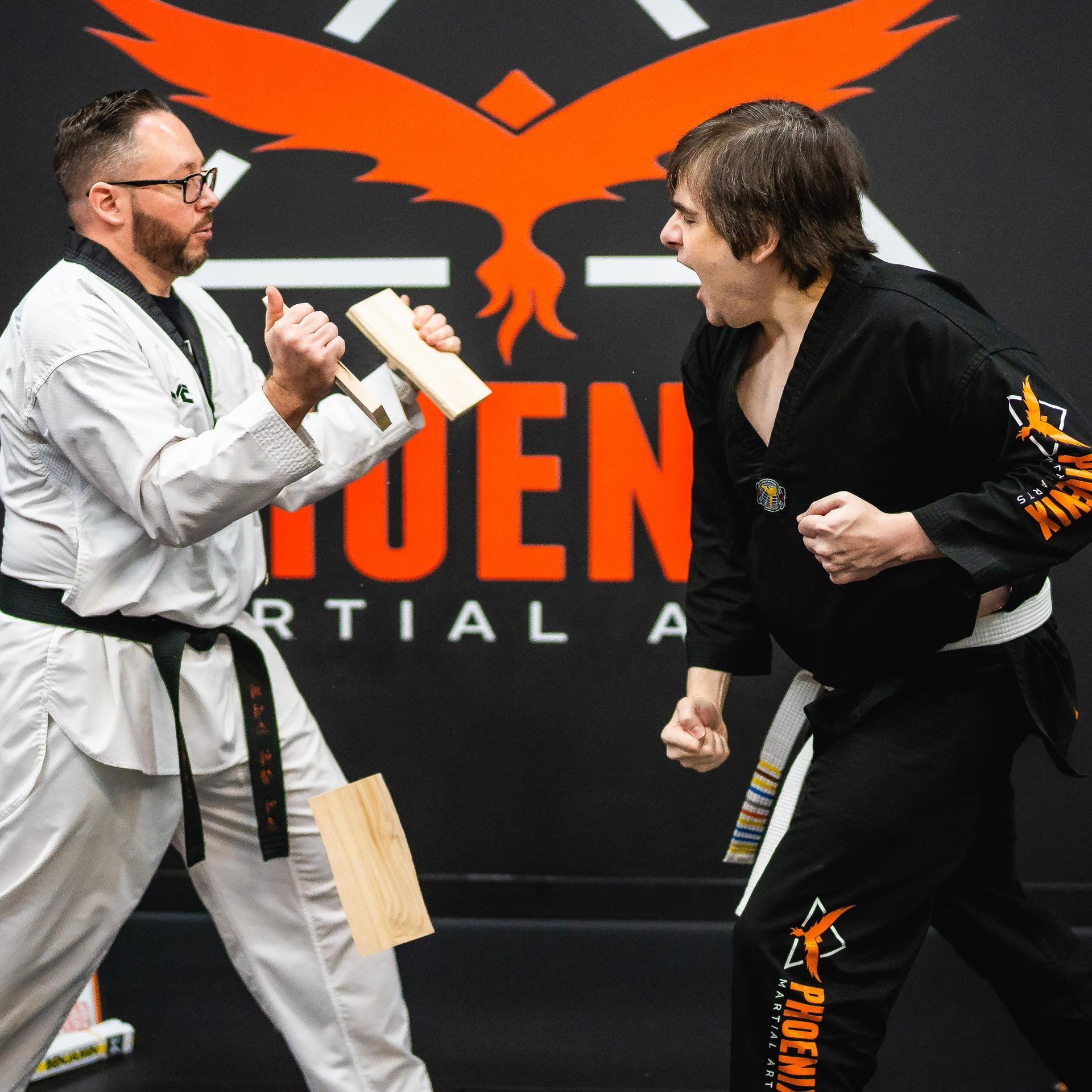 Two men are fighting in front of a phoenix martial arts logo