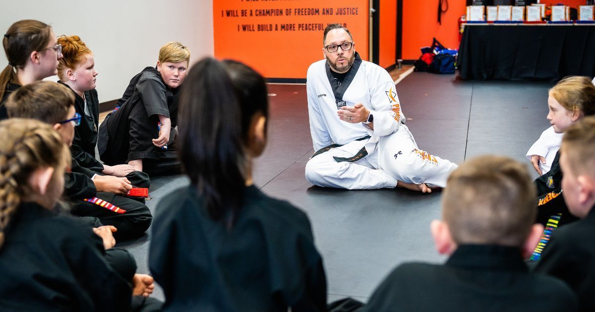 A group of children are sitting in a circle around a man in a karate uniform.