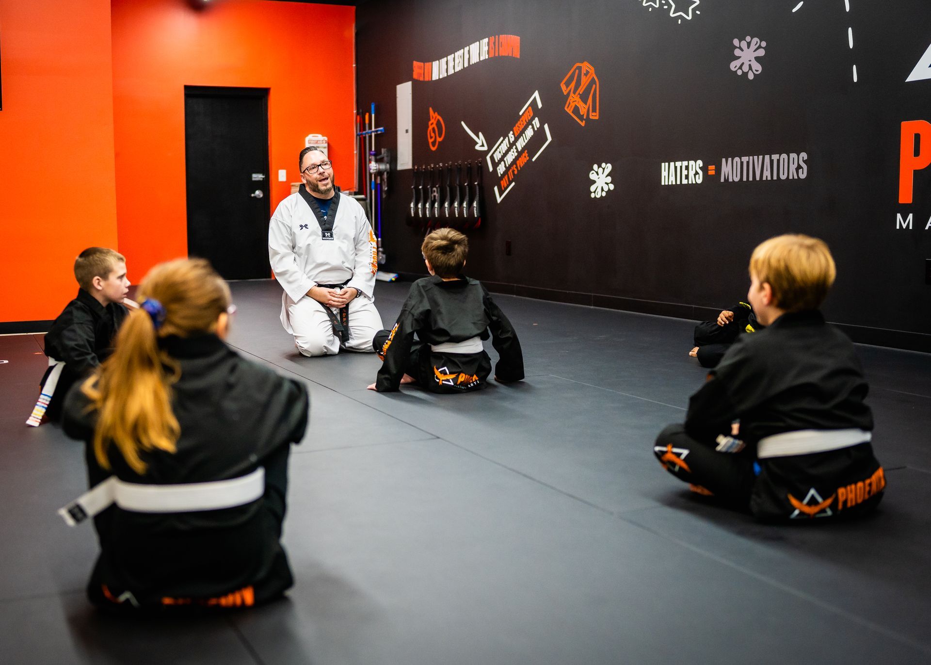 A group of children are sitting on a mat in a karate class.