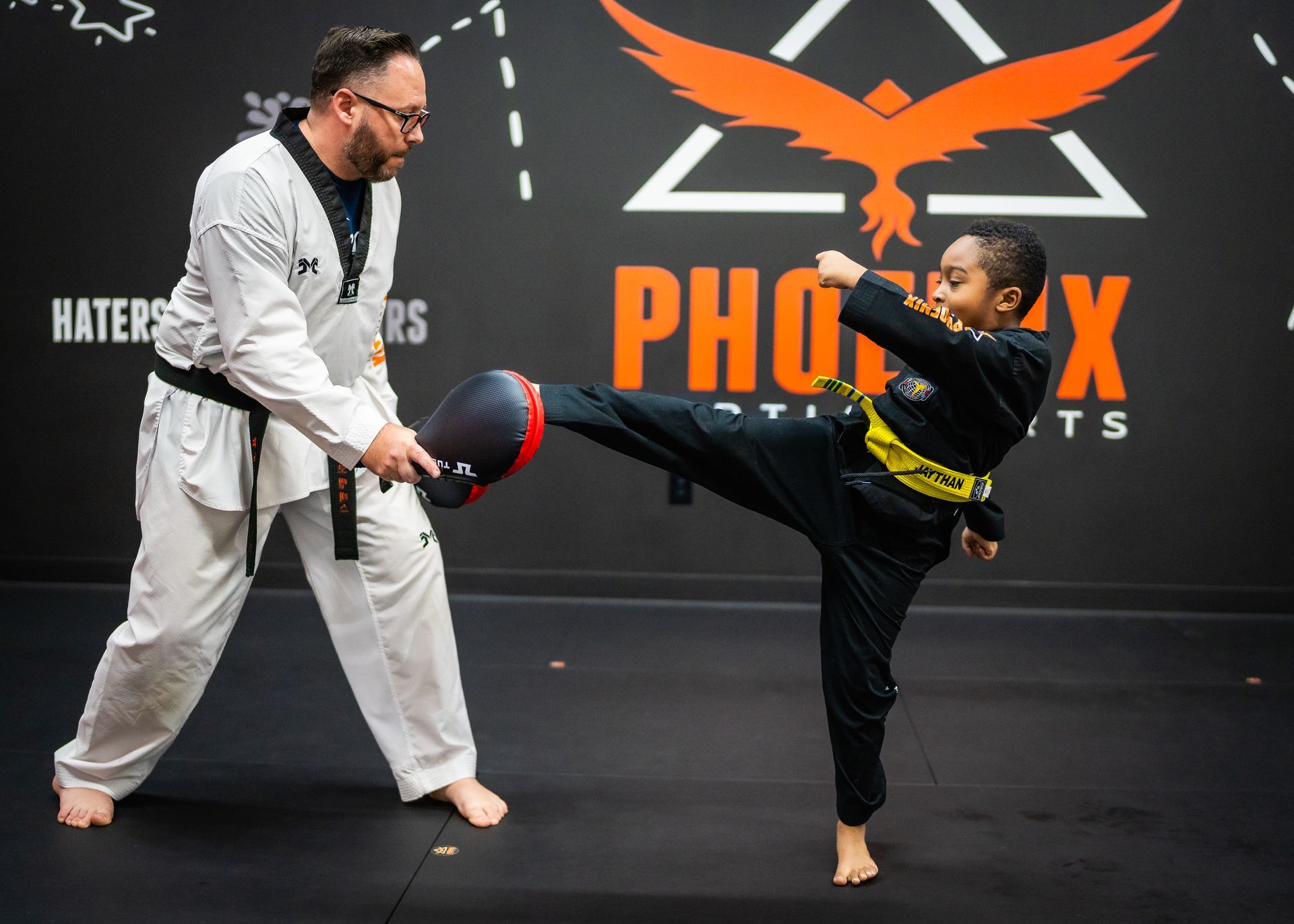 A man and a boy are practicing martial arts in front of a sign that says phoenix.