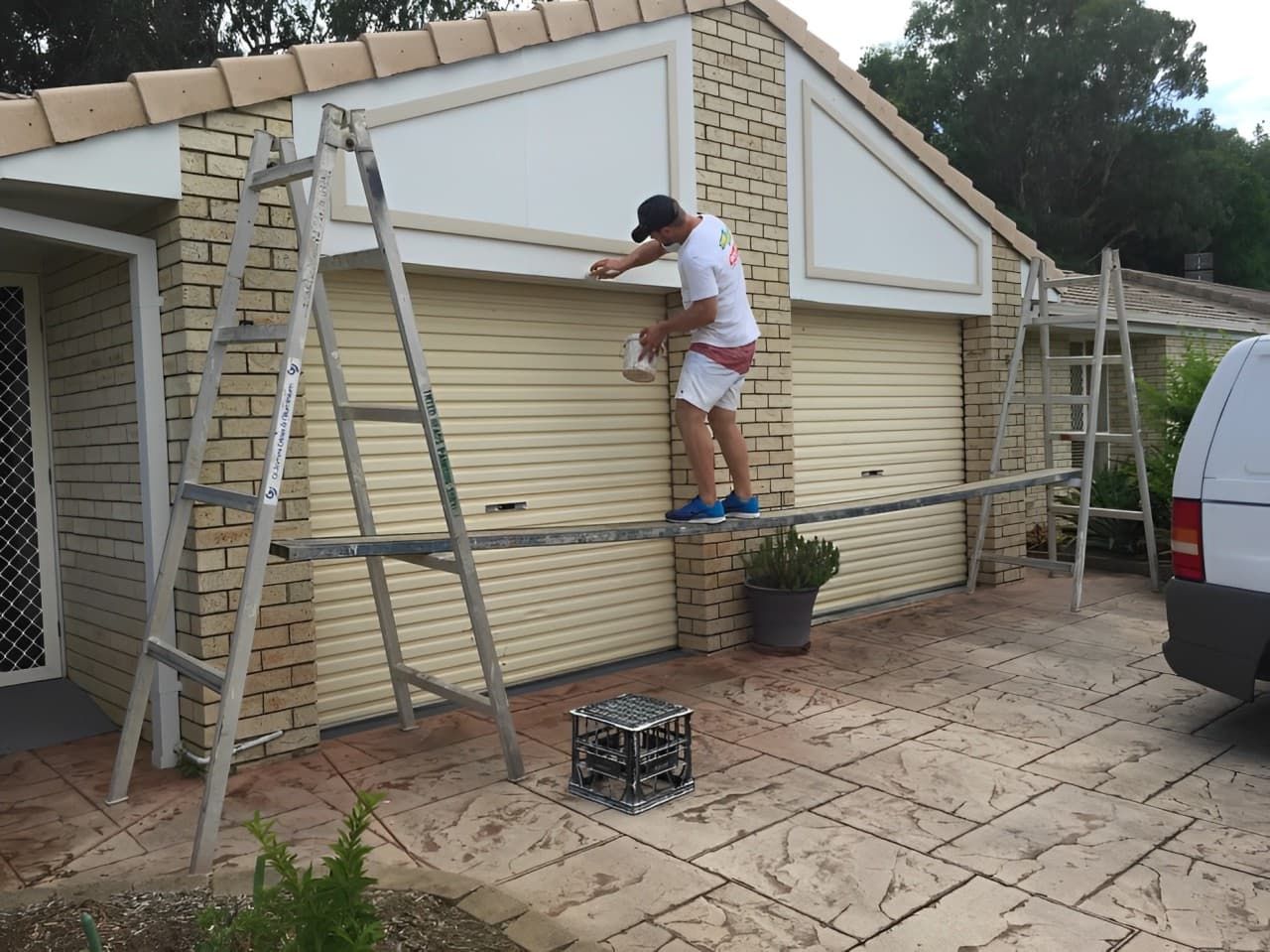 A Man Is Standing On A Ladder Painting A Garage Door — Tweed Heads Painting Service In Condong, NSW