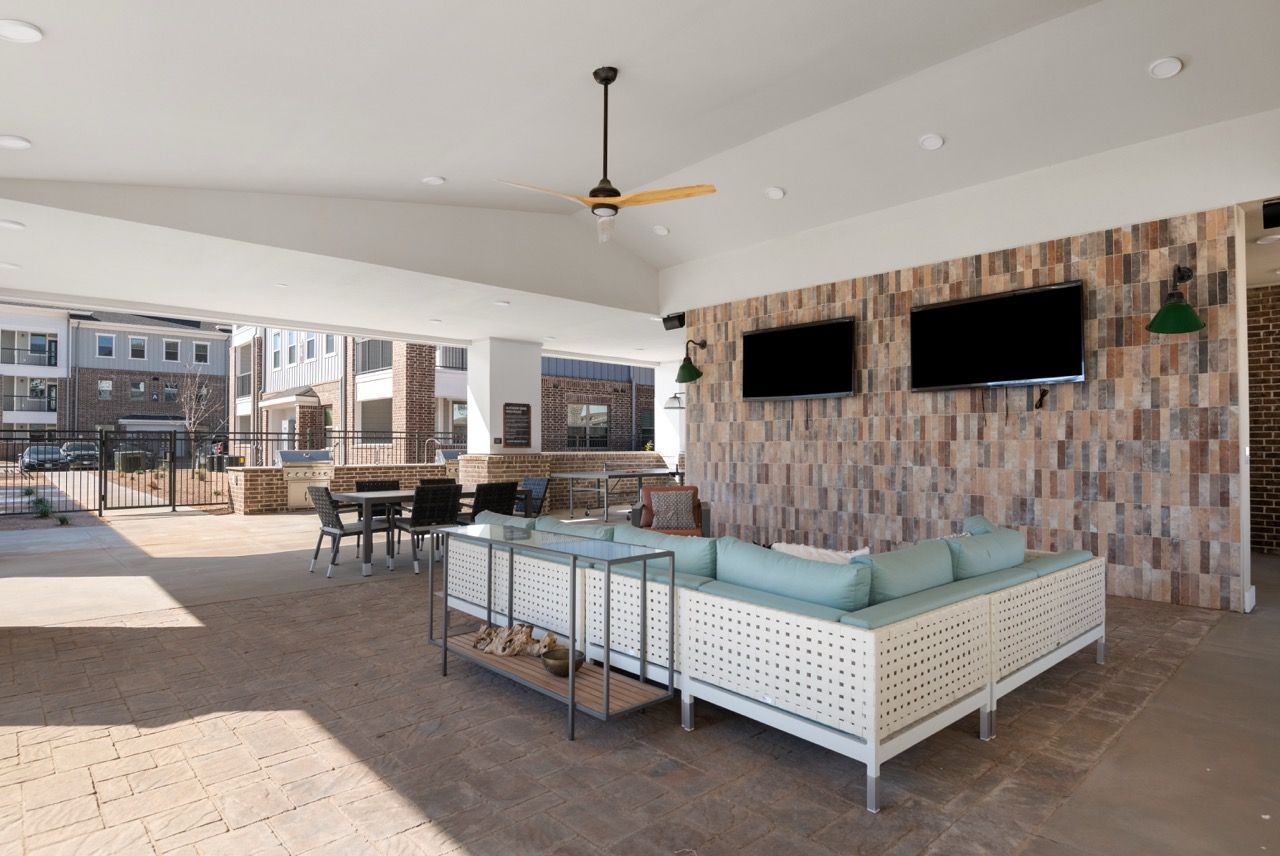 Covered outdoor community lounge with sectional seating, ceiling fan, and two wall-mounted TVs.