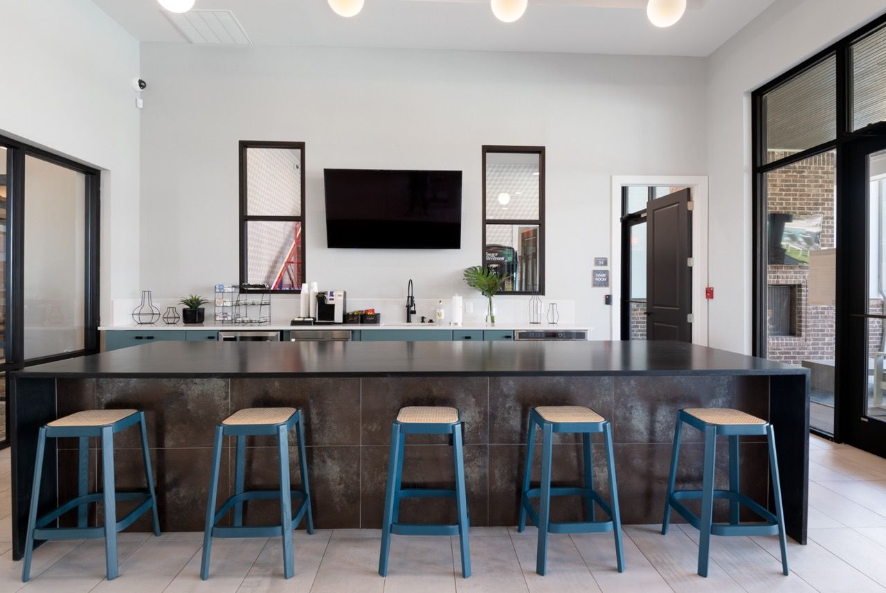 Interior of a modern community kitchen with a long dark island and teal stools.