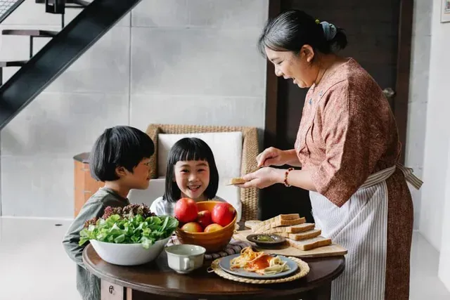 A woman is preparing food for two children at a table.