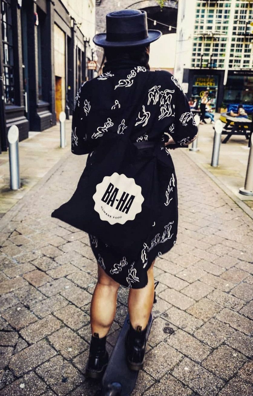 Person walking down a brick-paved alley, wearing a hat, patterned coat, and carrying a tote bag that says