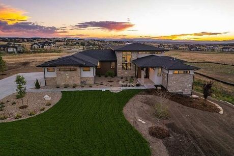 Modern stone house at sunset with green lawn and desert landscaping, seen from the front.