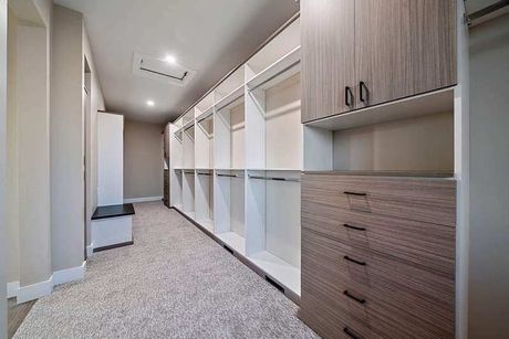 Spacious walk-in closet with white shelves, wood drawers, and carpeted floor