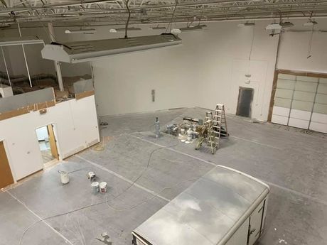 Large empty industrial warehouse with a white truck, scaffolding, and work materials on the floor