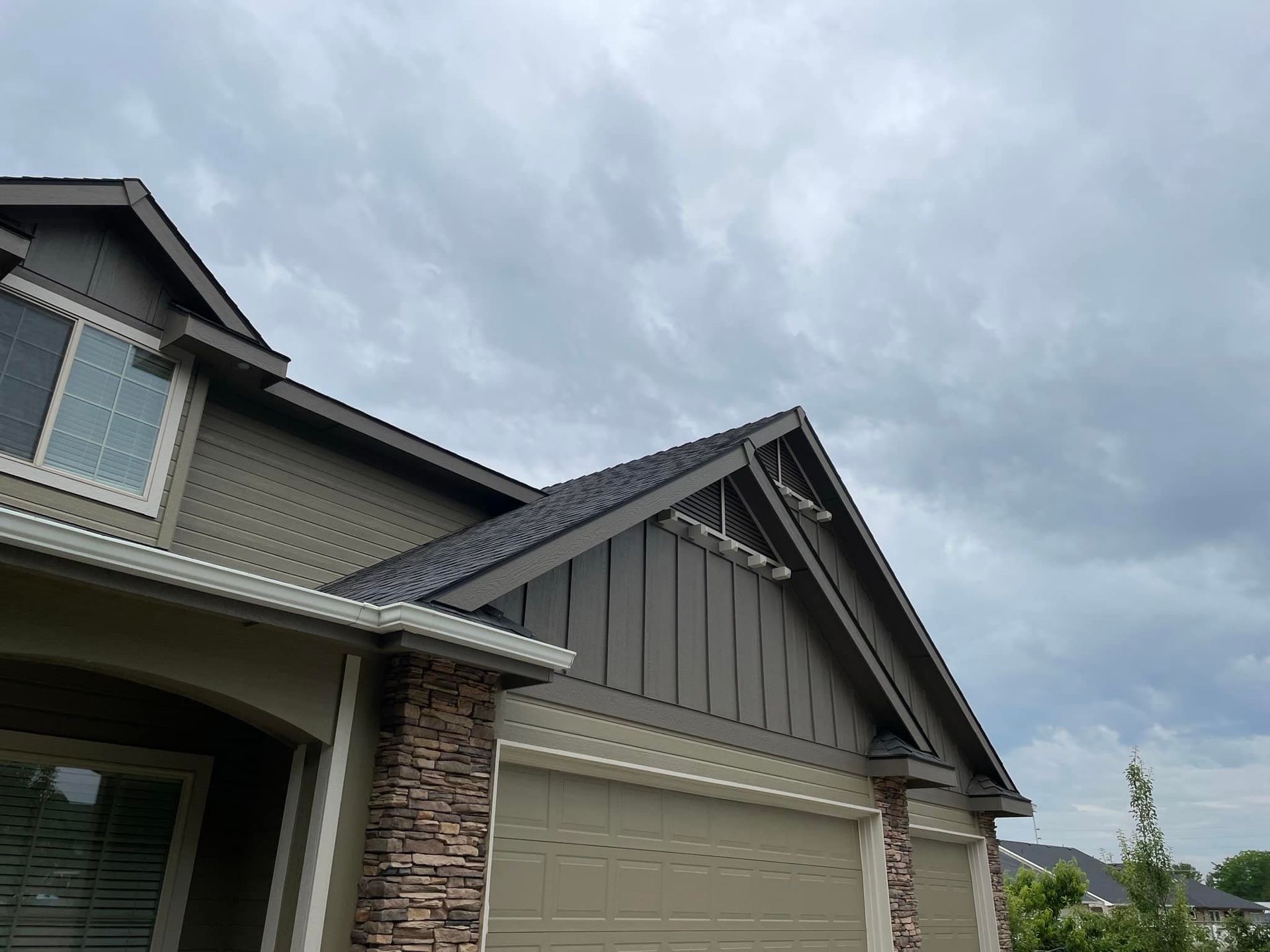 Suburban house exterior with gray siding, stone accents, and a cloudy sky