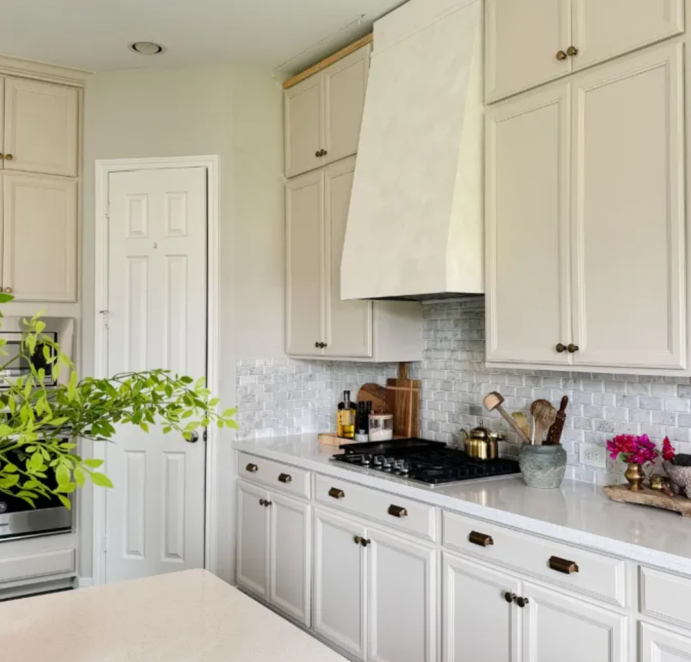 Bright white kitchen with shaker cabinets, marble countertops, and a black stove under a tiled backsplash.