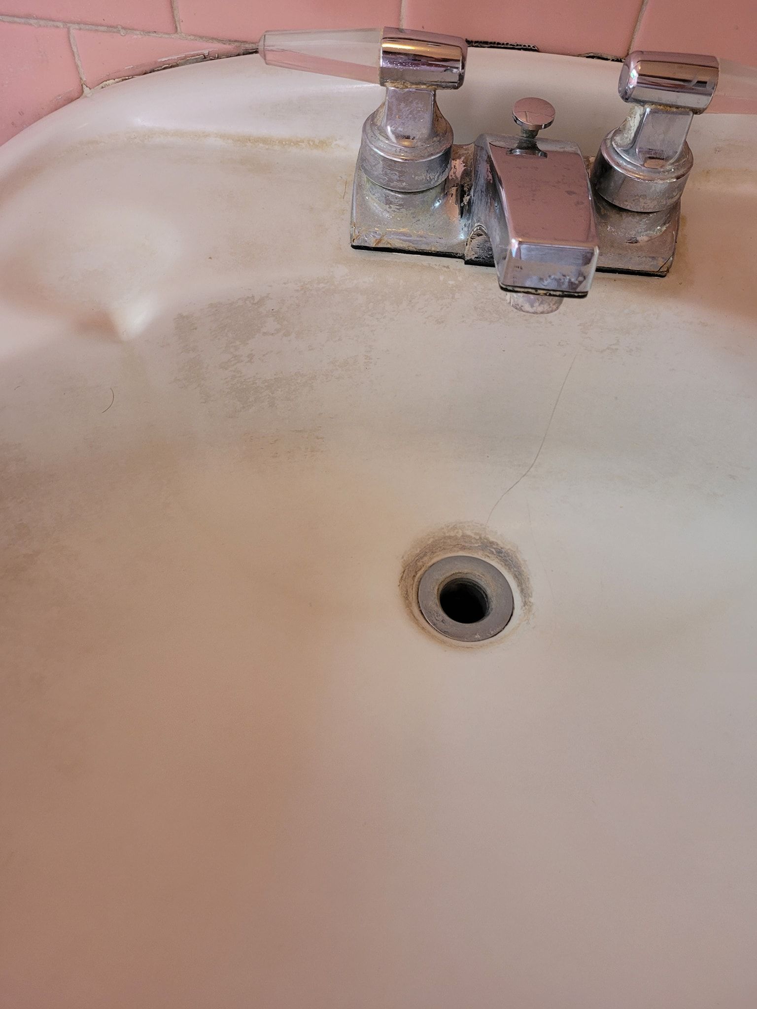 A close up of a bathroom sink with a pink tile wall.