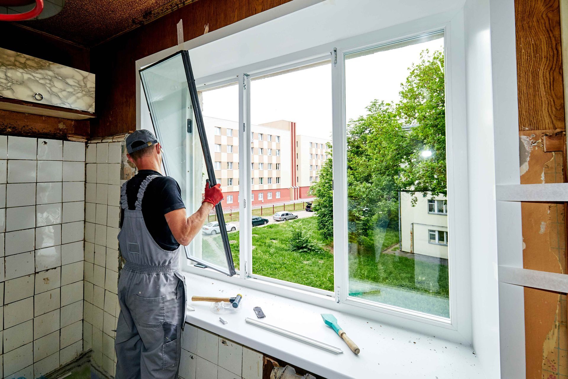 Technician installing large glass pane during window replacement in modern home interior. Technician installing large glass pane during window replacement in modern home interior.