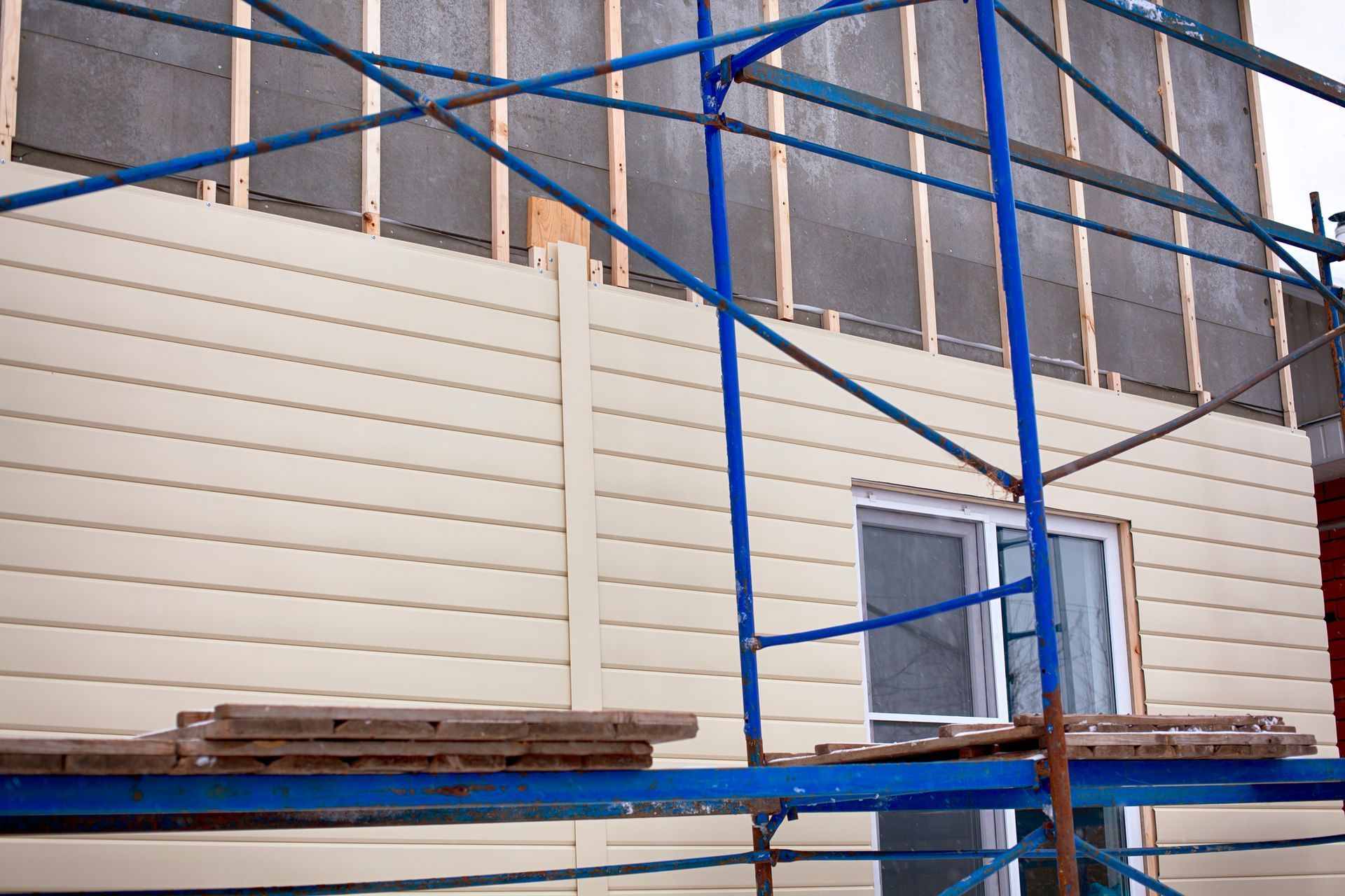 Construction scaffolding surrounding a house being upgraded with beige exterior siding.