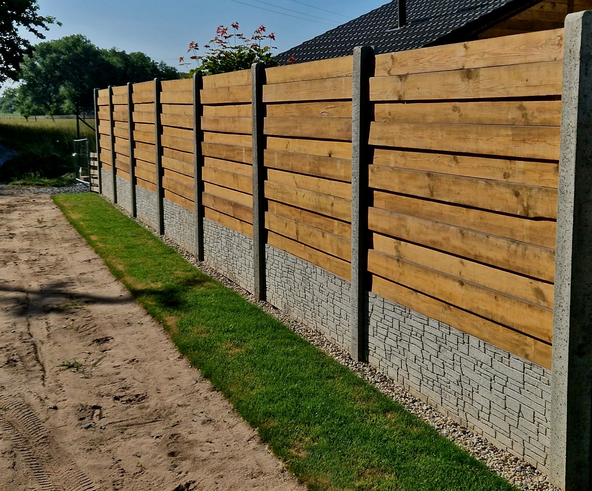 A wooden fence along a dirt road in front of a house