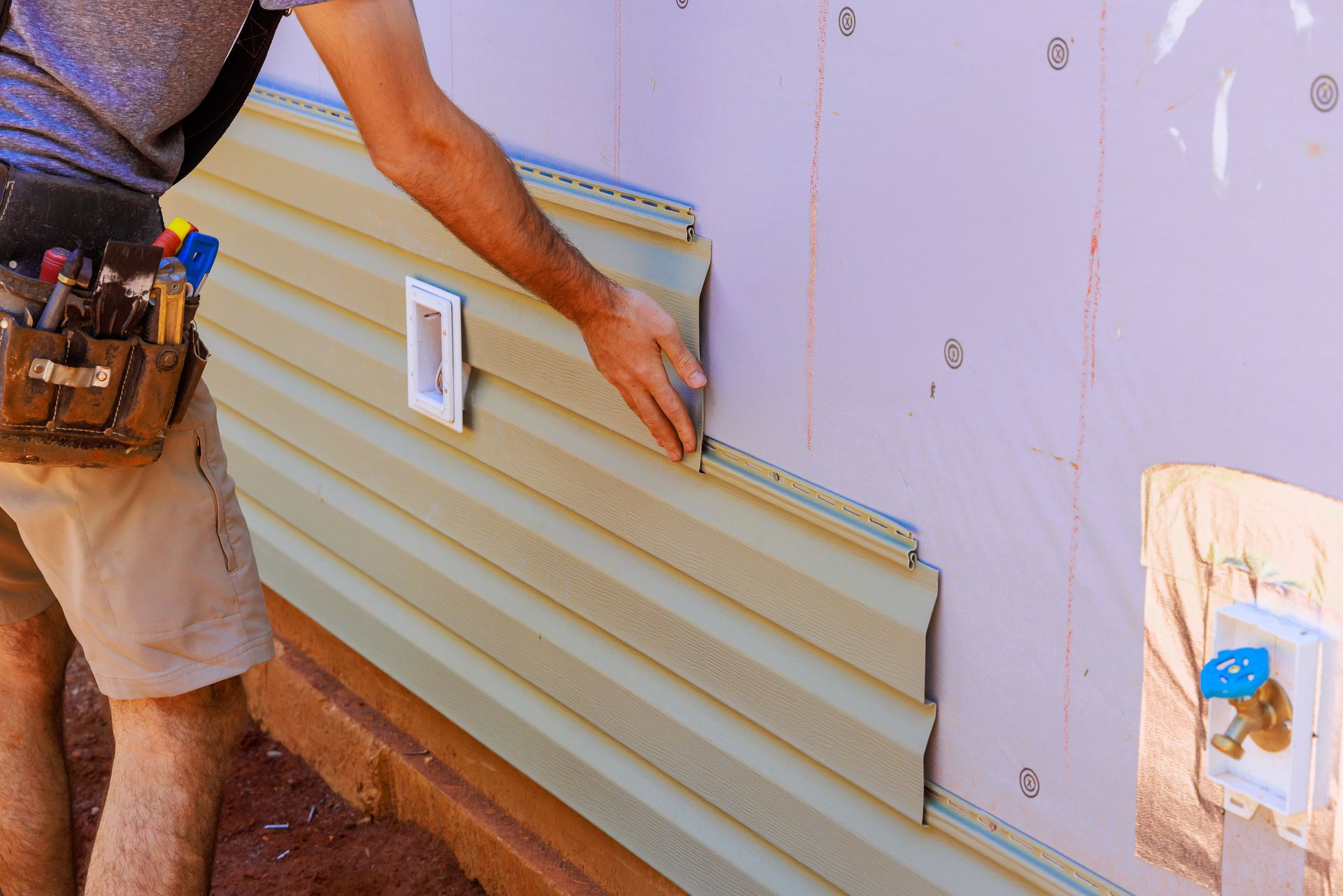 A worker installs vinyl plastic siding panels on the wall facade of a residence. A worker installs vinyl plastic siding panels on the wall facade of a residence.