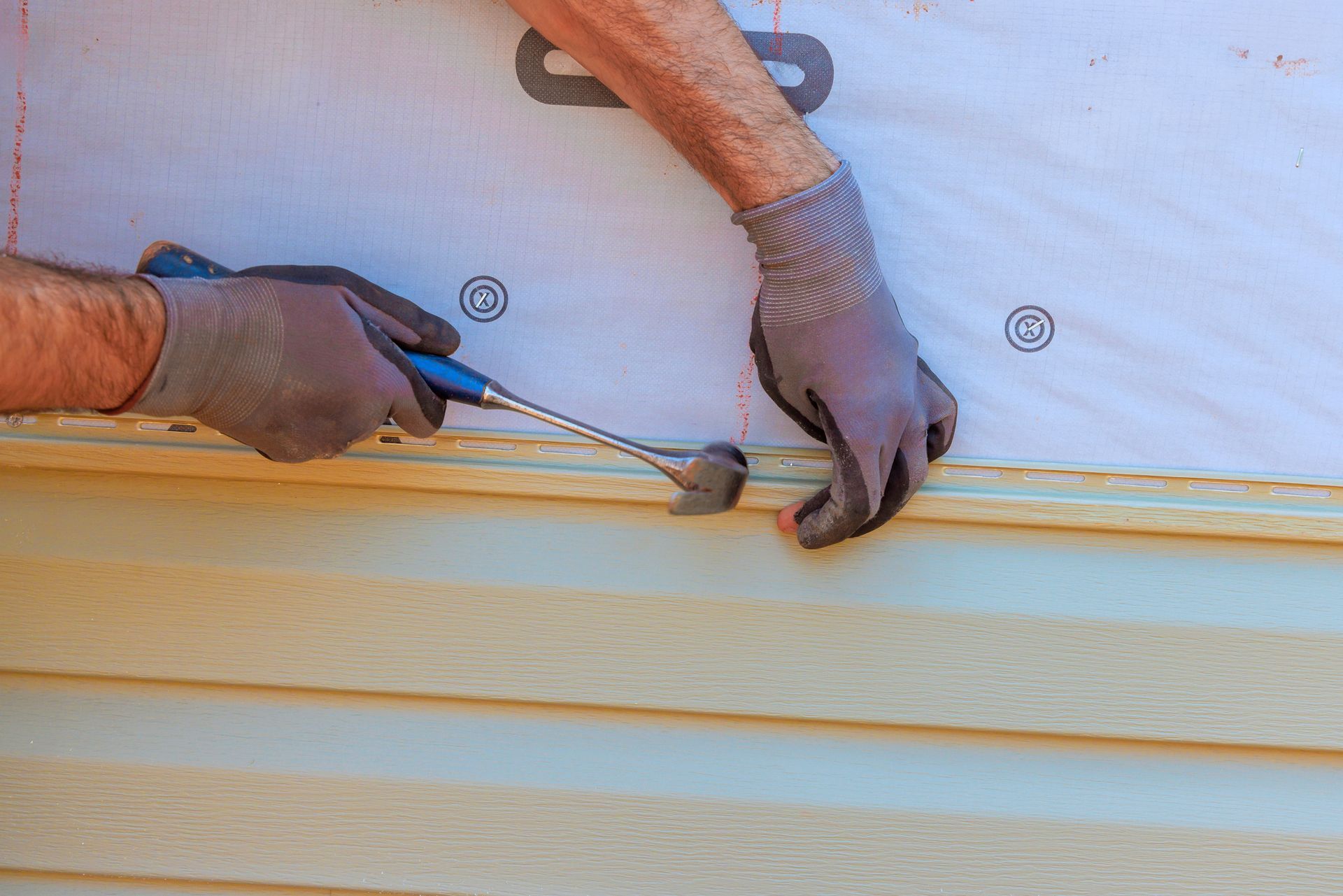 A contractor carefully secures trim to new exterior vinyl siding.