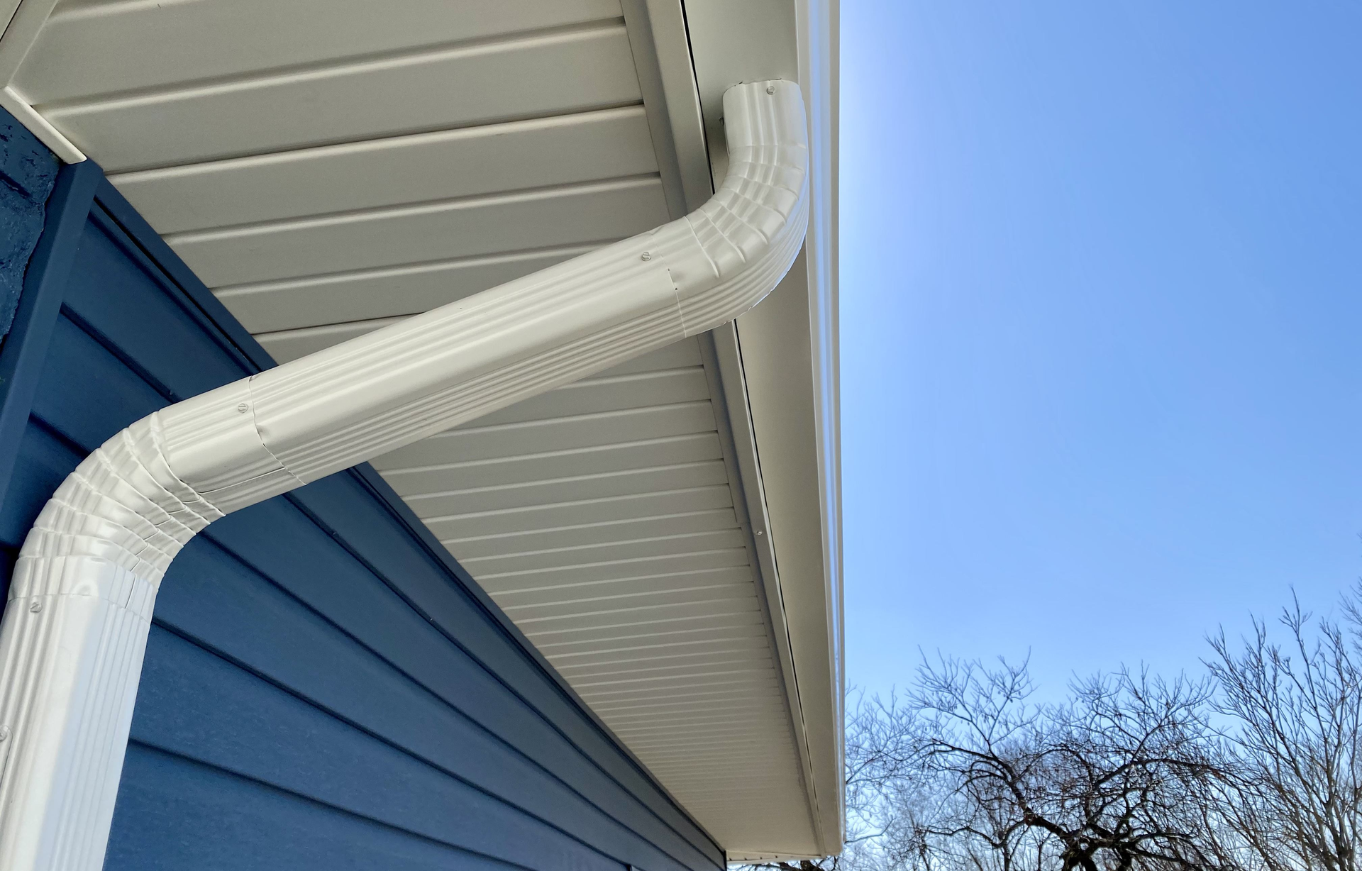 A white gutter is attached to the side of a blue house | Siefken Roofing and Remodeling Services in Omaha, NE