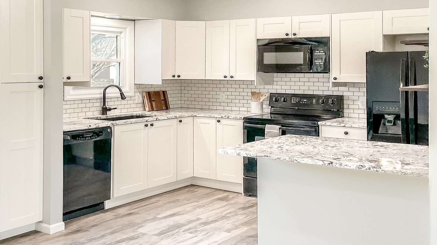 A kitchen with white cabinets , black appliances and granite counter tops | Siefken Roofing and Remodeling Services in Omaha, NE