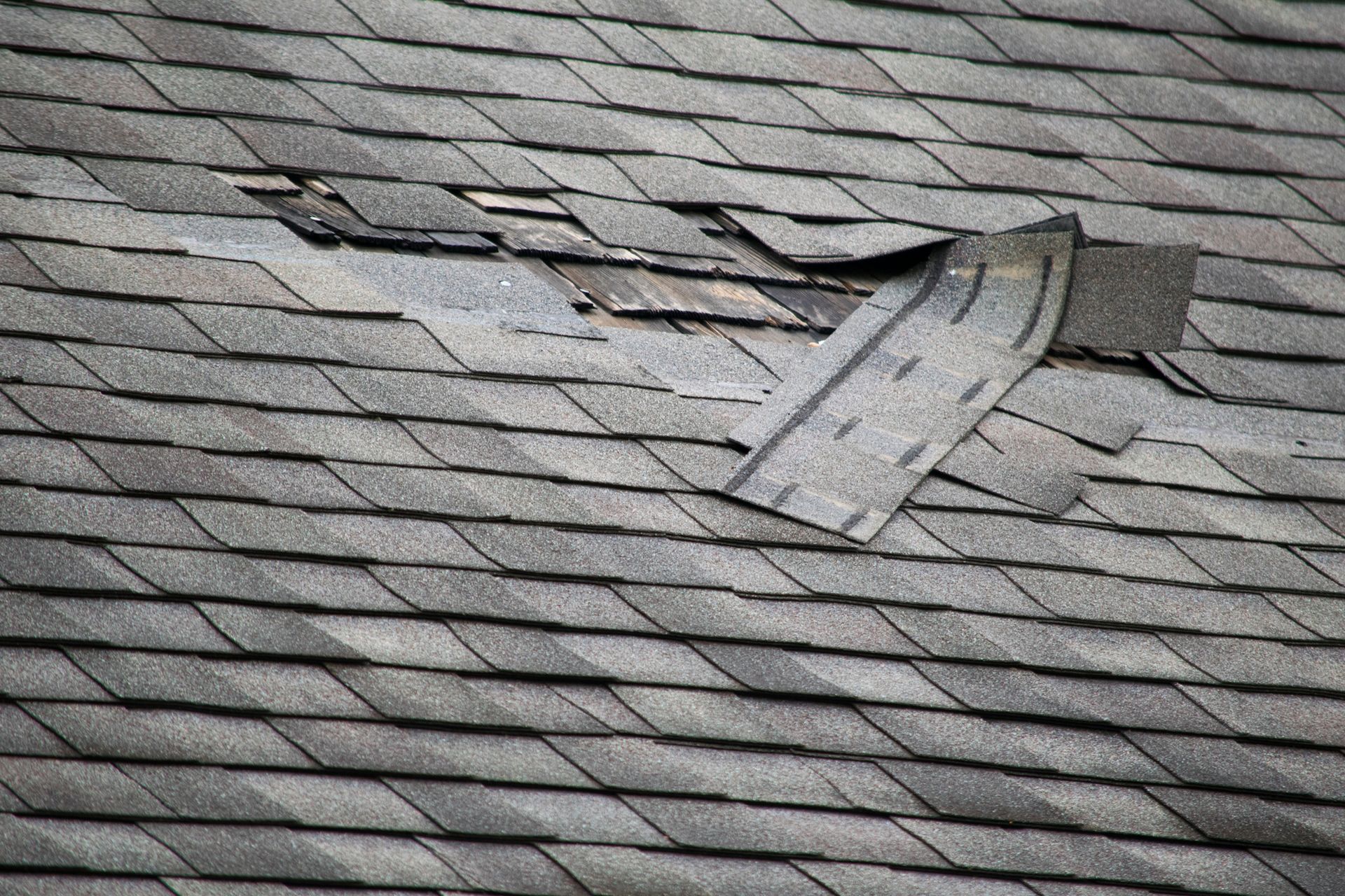 Close-up view of a roof with missing and damaged shingles.