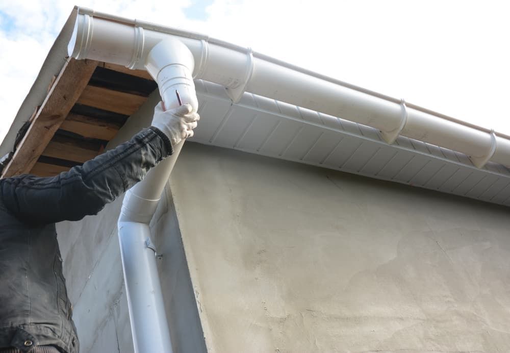 A Person Is Installing a Gutter on The Side of A House — South Coast Gutter Wiz in Sanctuary Point, NSW