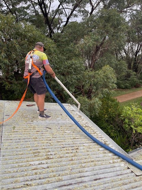 A Man Is Cleaning a Roof with A High Pressure Washer — South Coast Gutter Wiz in Ulladulla, NSW