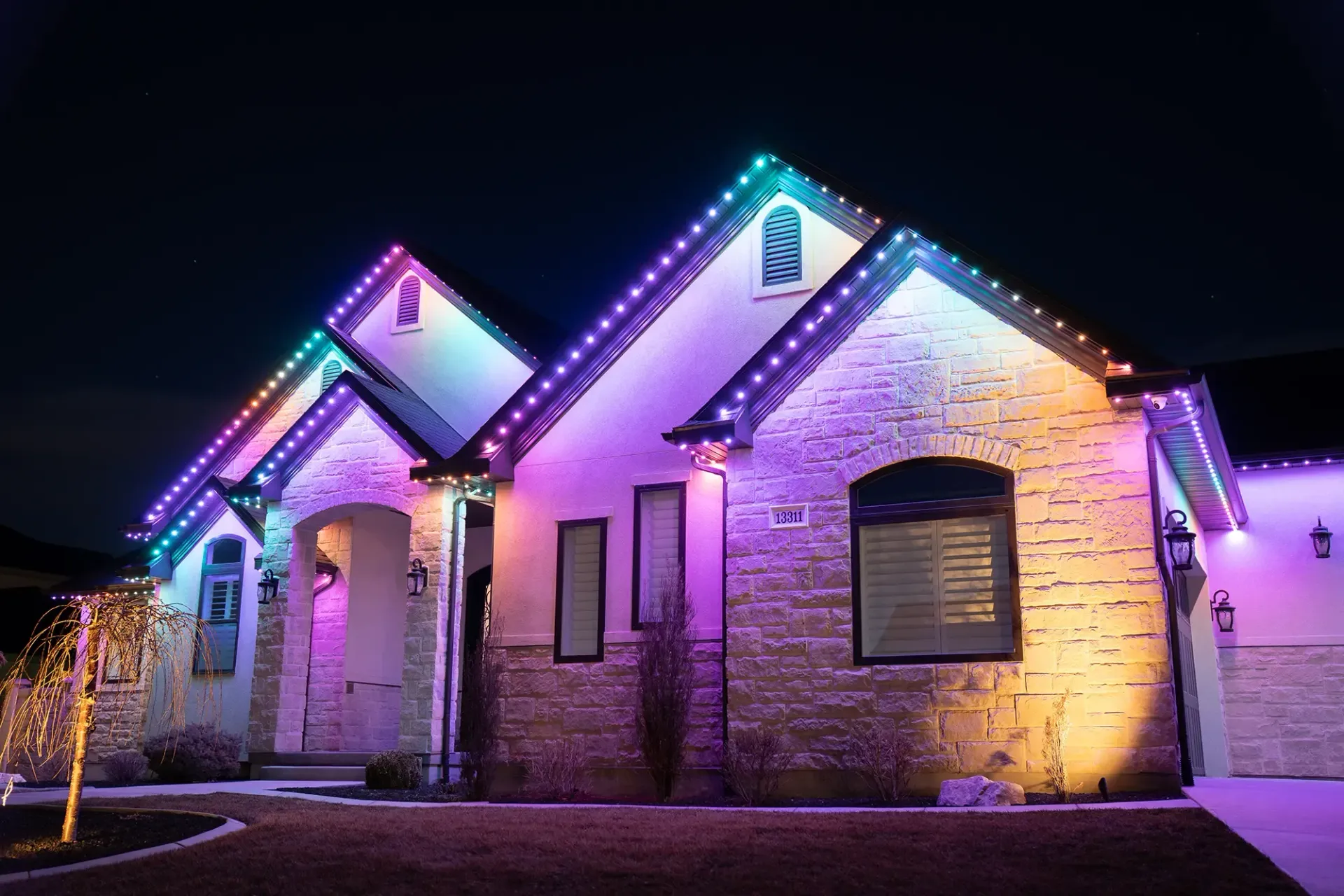House lit with colorful Christmas lights, roof and exterior walls illuminated in pink, blue, green, and yellow.