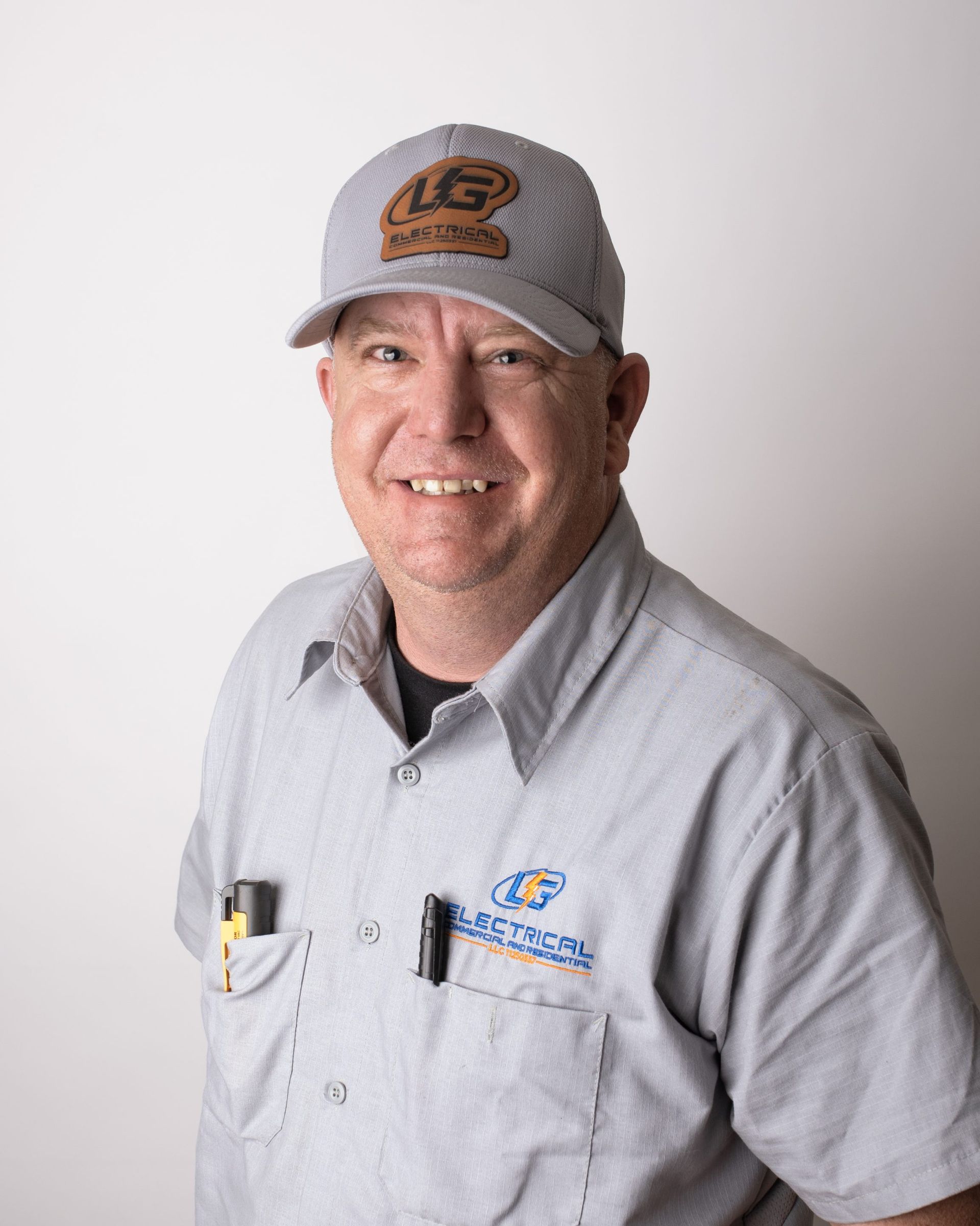 Man in gray work shirt and cap, smiling at the camera. He has a tool in his pocket.