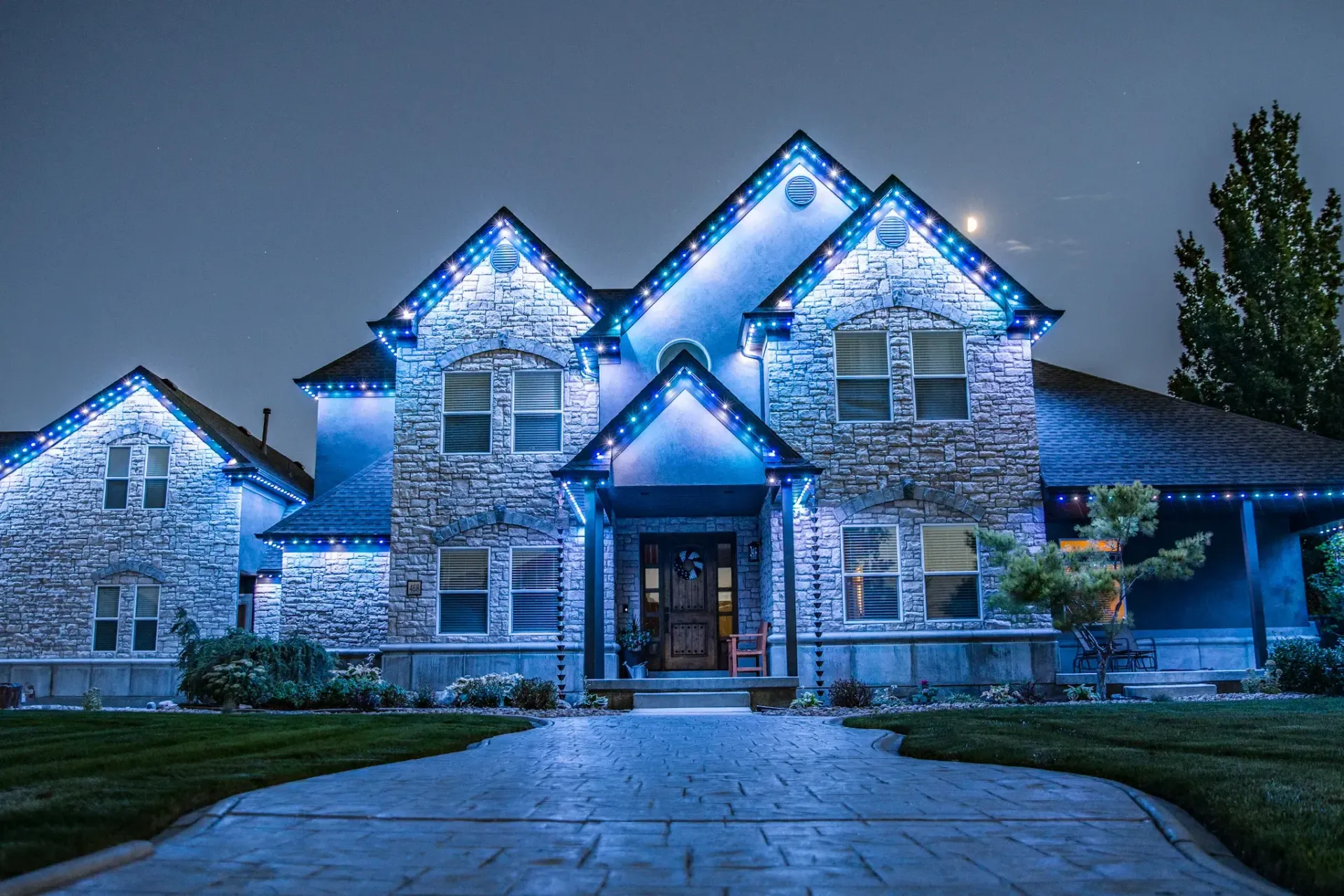 House exterior at night, lit with blue Christmas lights along roofline and driveway.