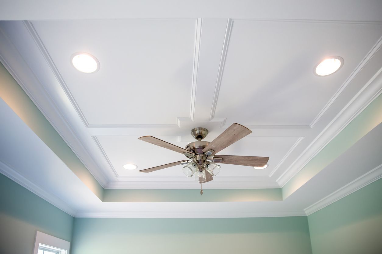 A ceiling with a fan and recessed lighting, white trim on a green-walled room.