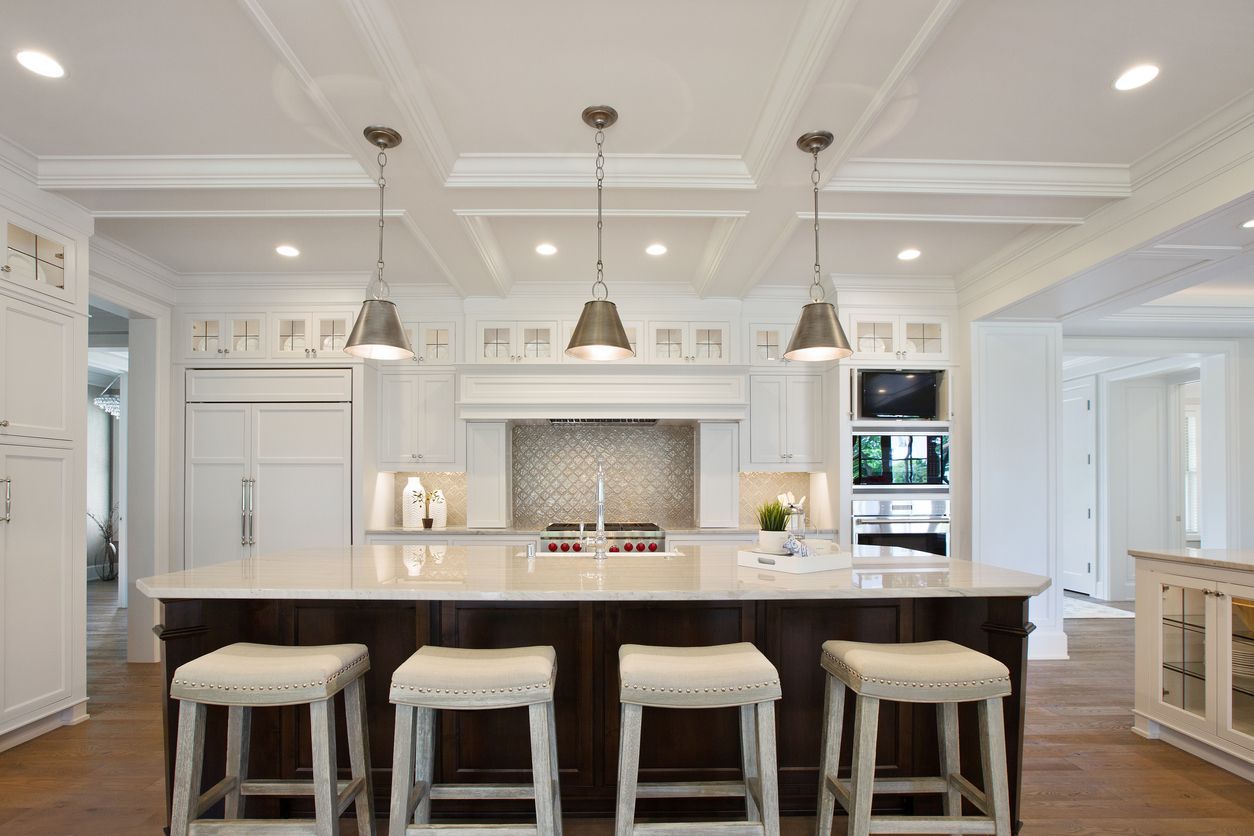 Kitchen with island, pendant lights, dark wood cabinets, white countertops, and four bar stools.