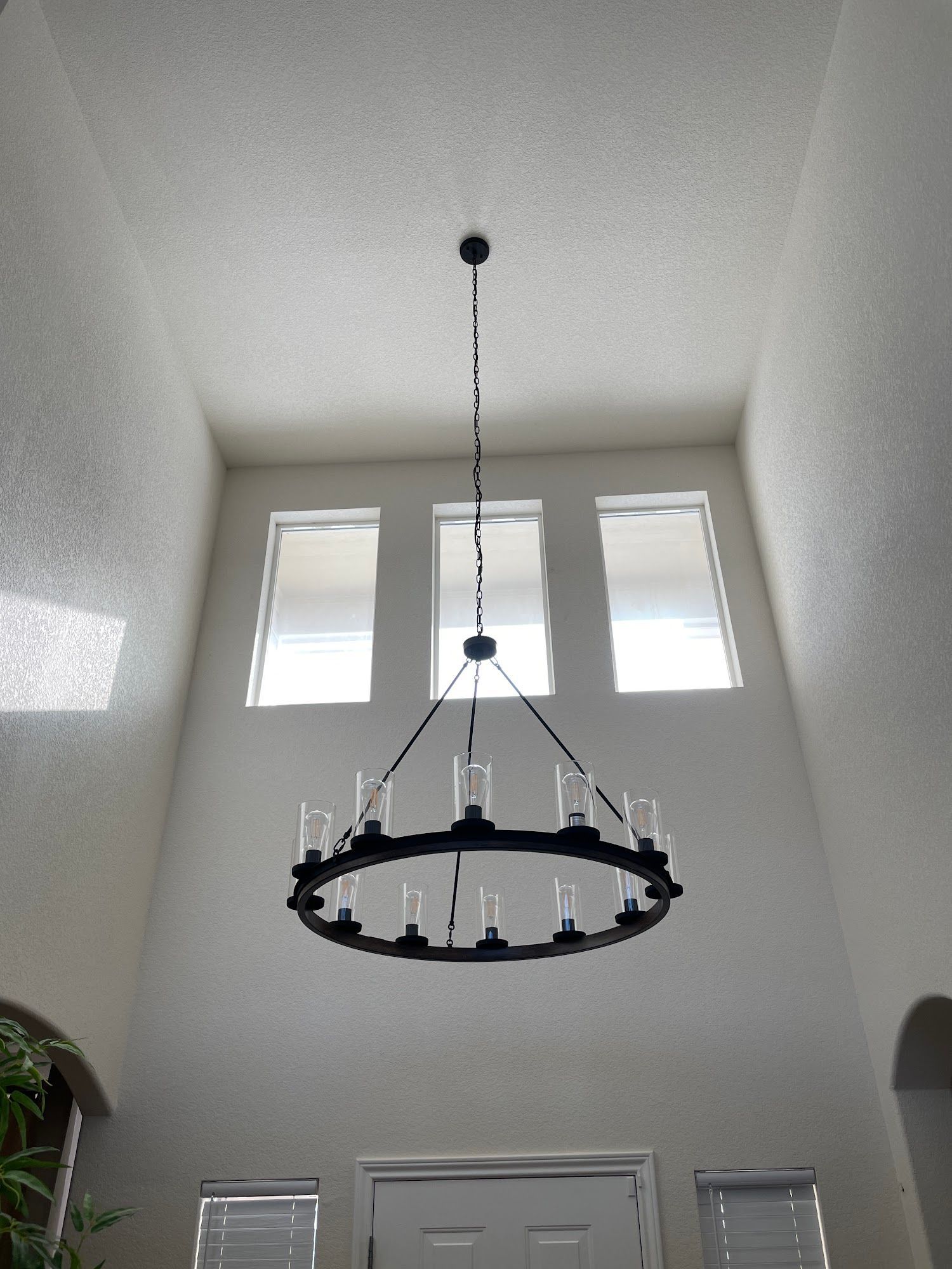 Tall entryway with a black chandelier, three windows, and a white door.