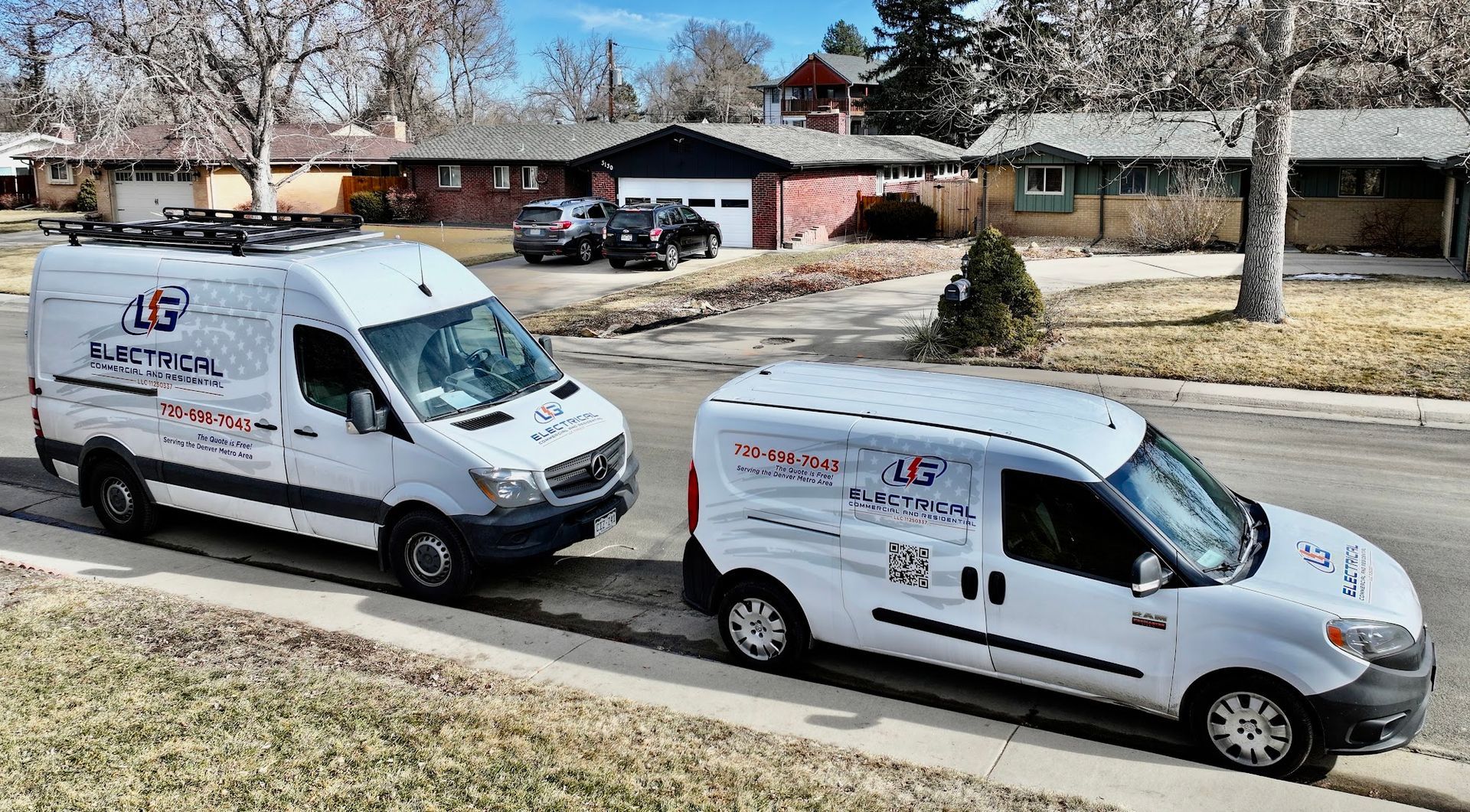 Two white work vans parked on a residential street. Both have company logos. Houses in the background.
