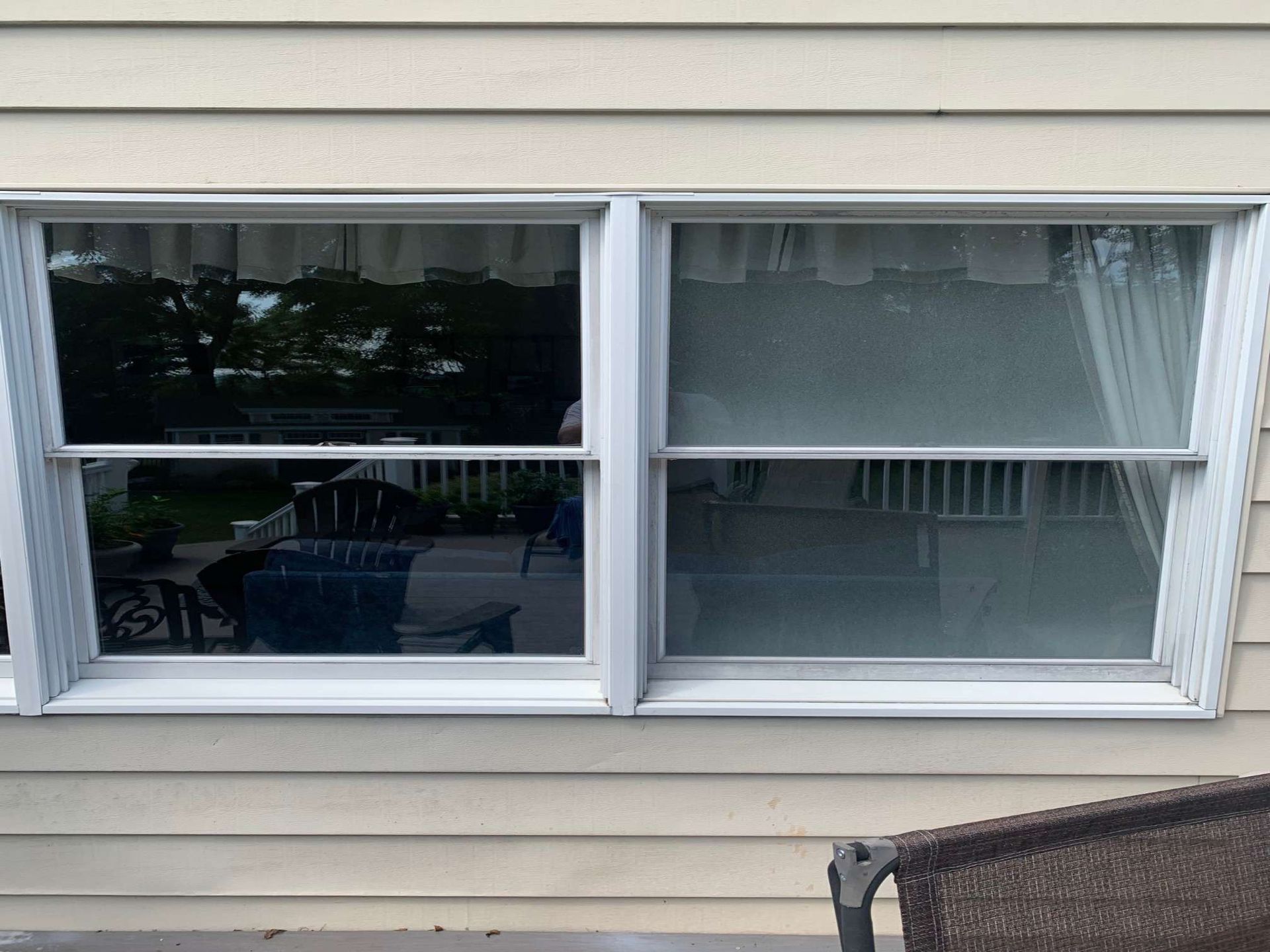 Two side-by-side single-hung windows with white frames on a beige, horizontal-sided house wall.