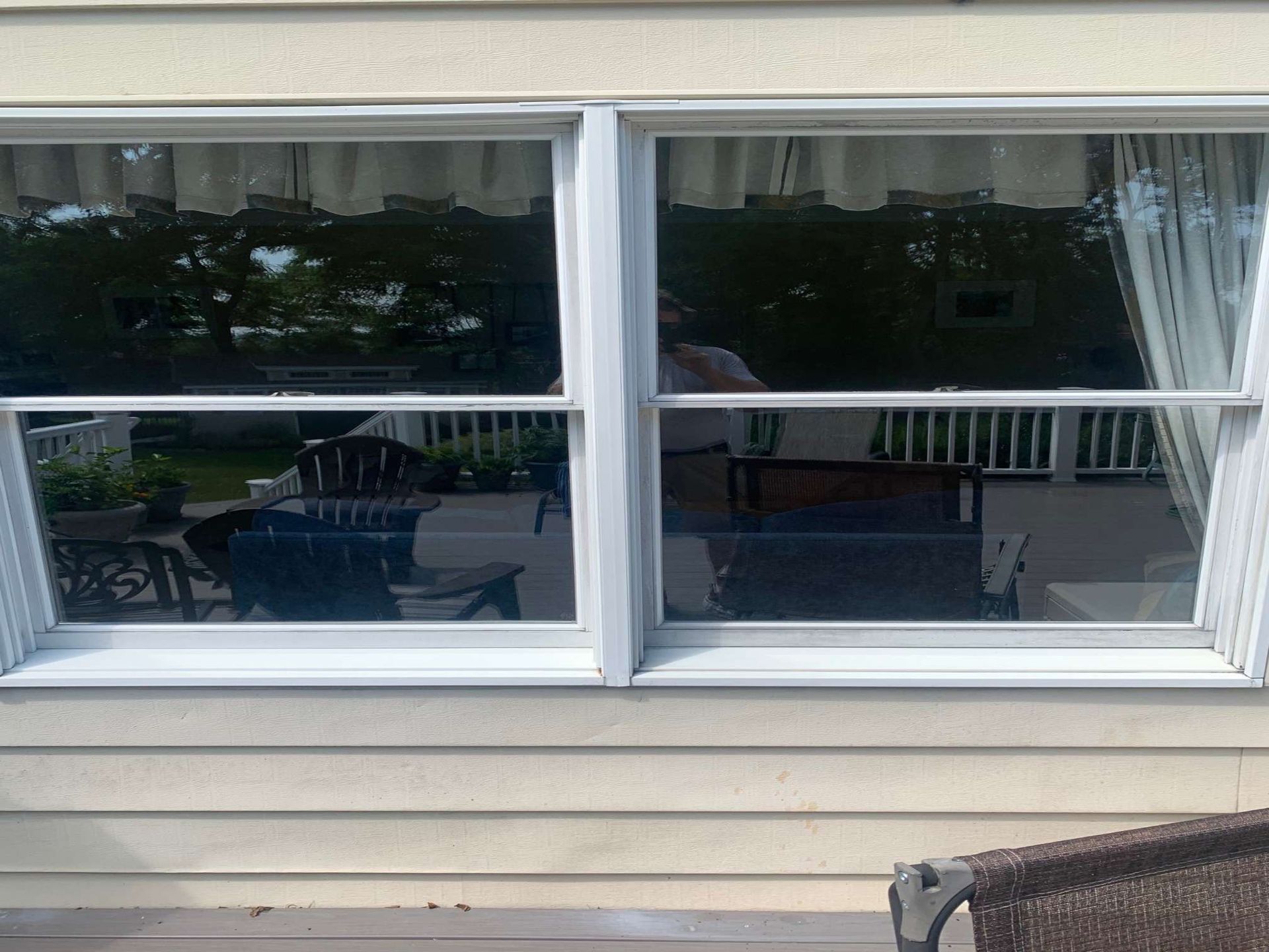 Two side-by-side single-hung windows with white frames on a beige exterior wall, reflecting an outdoor patio area.